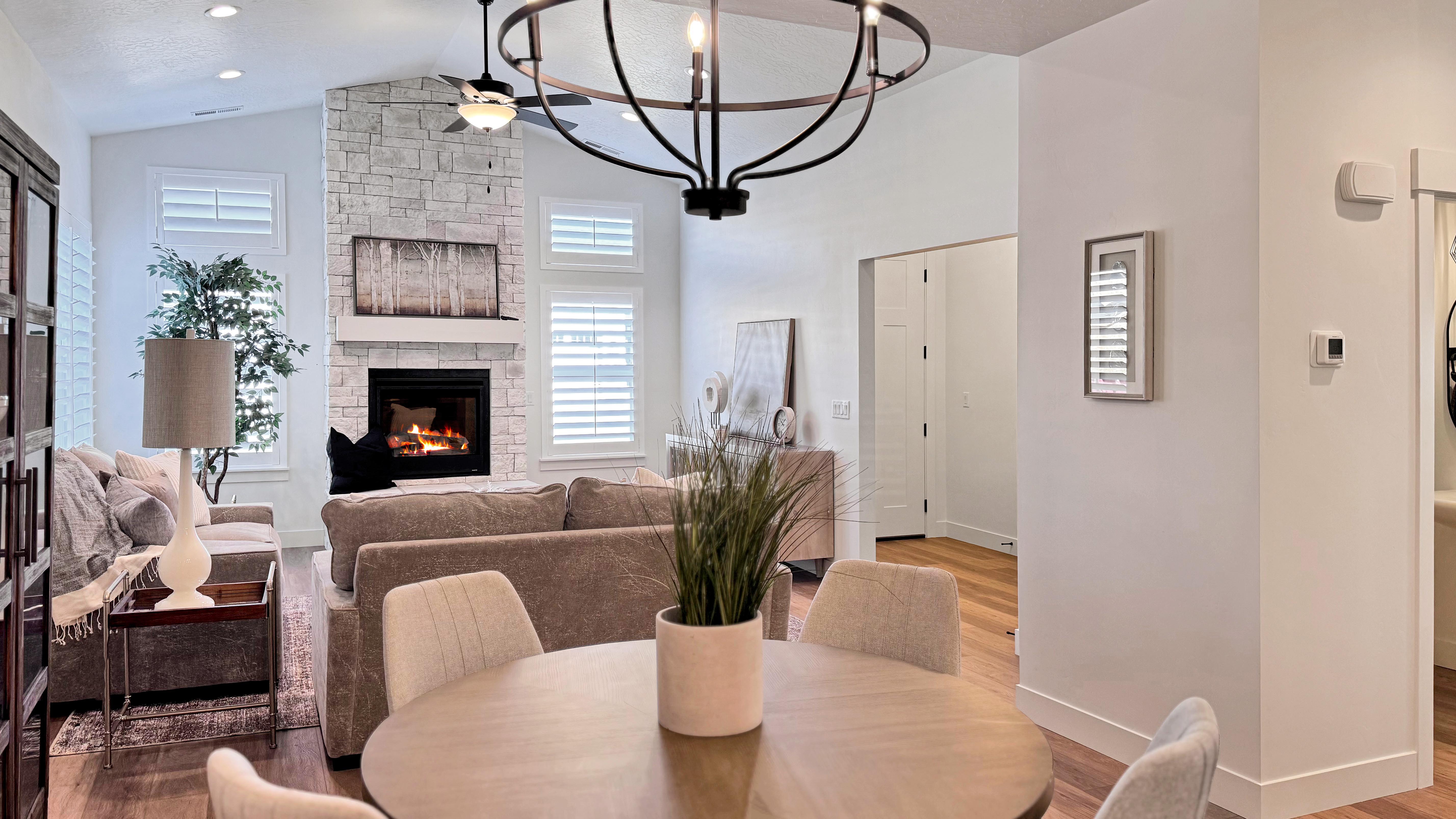 Open-concept living space featuring a stacked stone fireplace with a white mantel, high vaulted ceilings, and wood-finish flooring