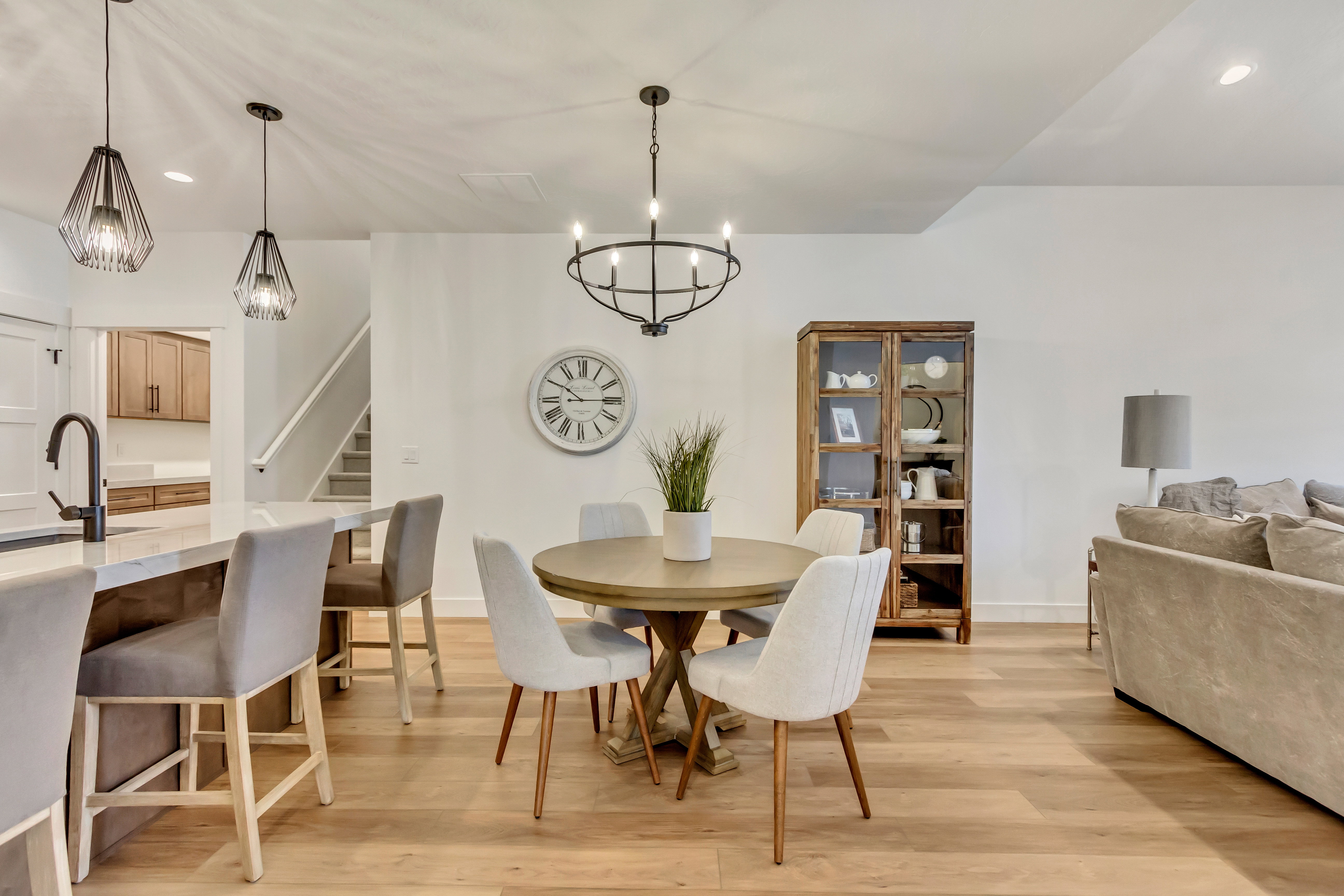 Open-concept living area with light wood-finish flooring, a kitchen island featuring pendant lighting and a black faucet, and a dining area illuminated by a circular chandelier