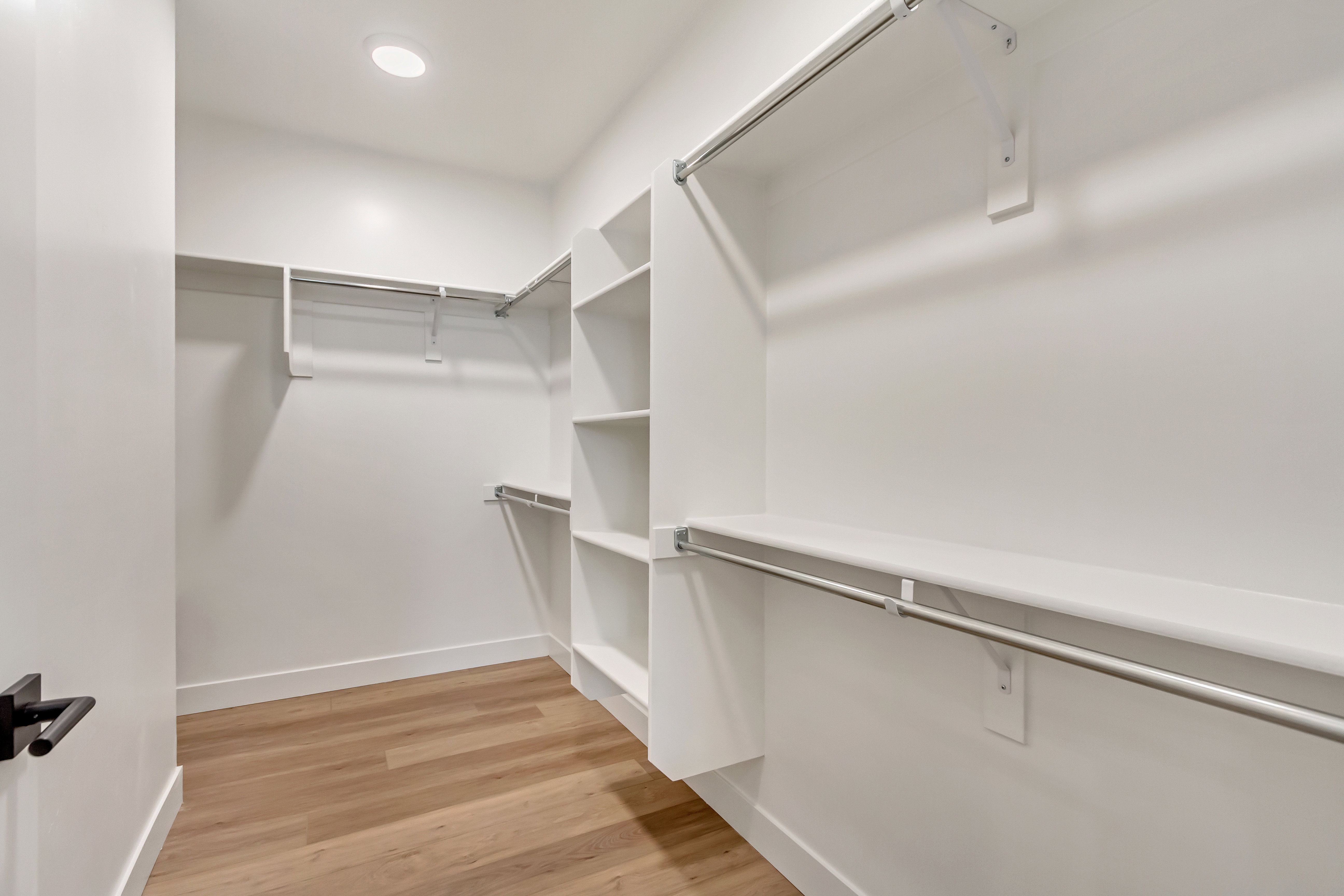 Spacious walk-in closet featuring wood-finish flooring, recessed lighting, white built-in shelving, and multiple chrome hanging rods for optimized organization
