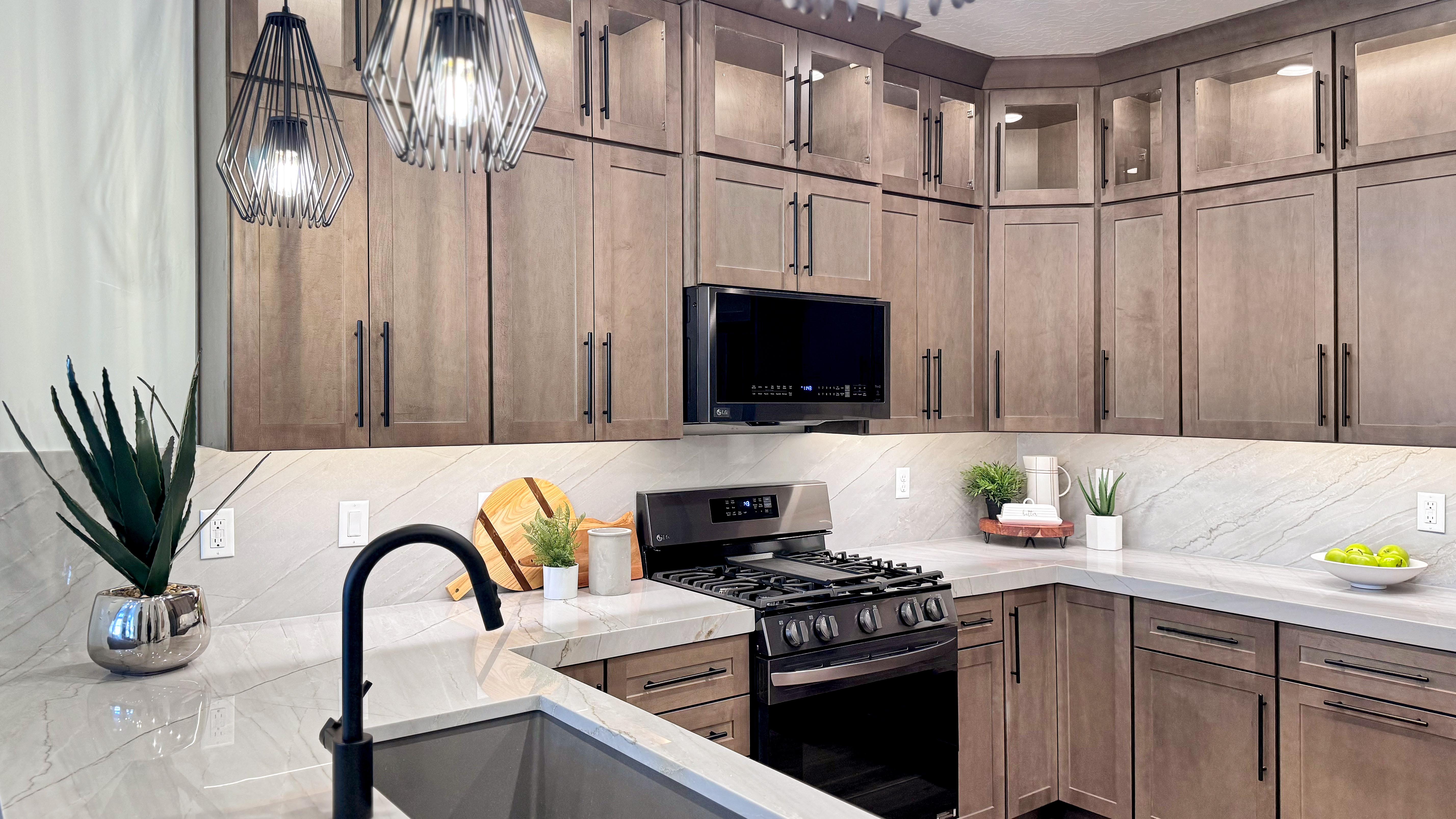 Modern kitchen featuring wood-finish cabinetry with dark hardware, light countertops with a matching backsplash, and geometric pendant lighting