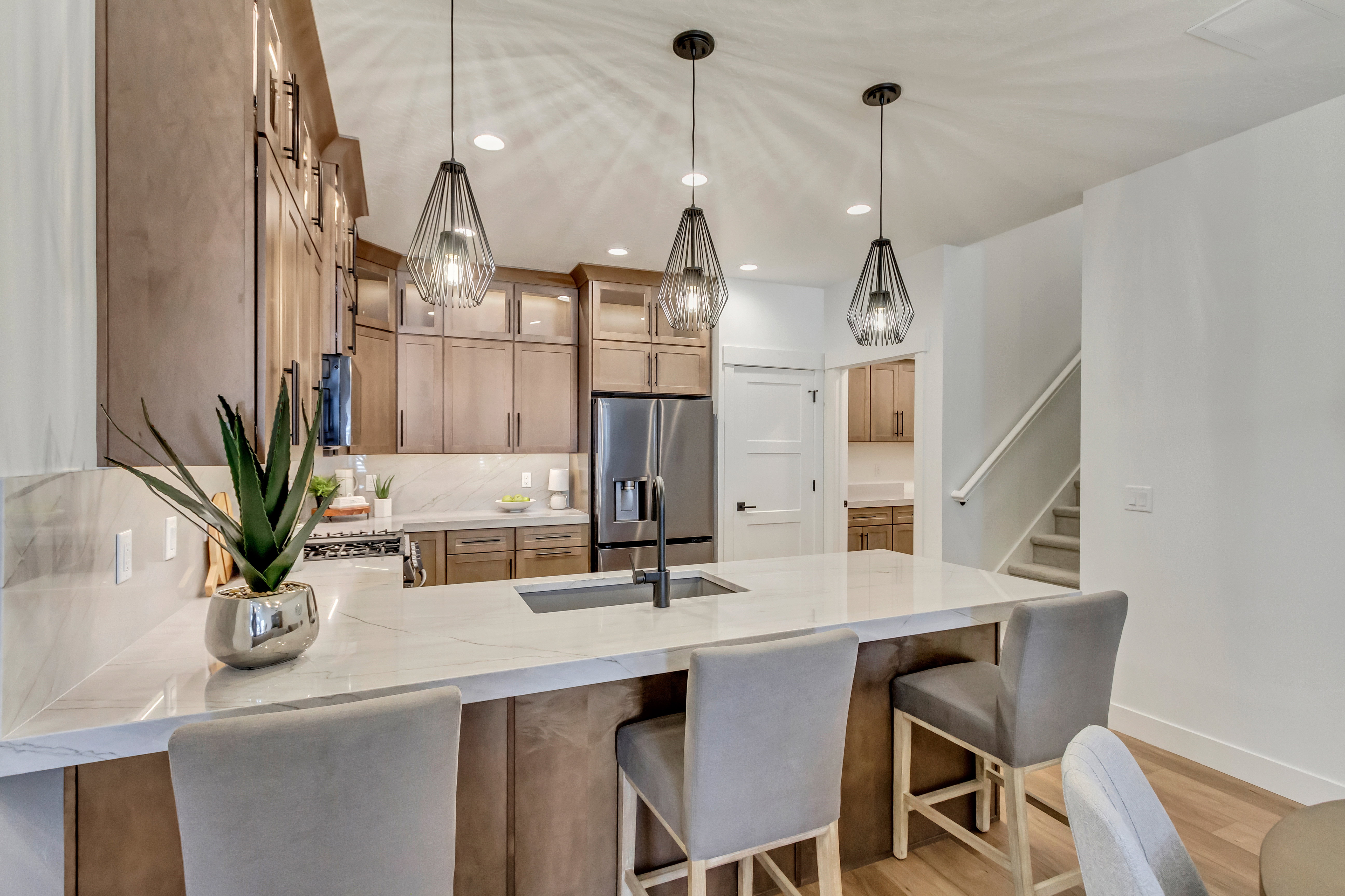 Modern kitchen featuring a waterfall island with an undermount sink, three geometric pendant lights, and light wood-finish cabinetry