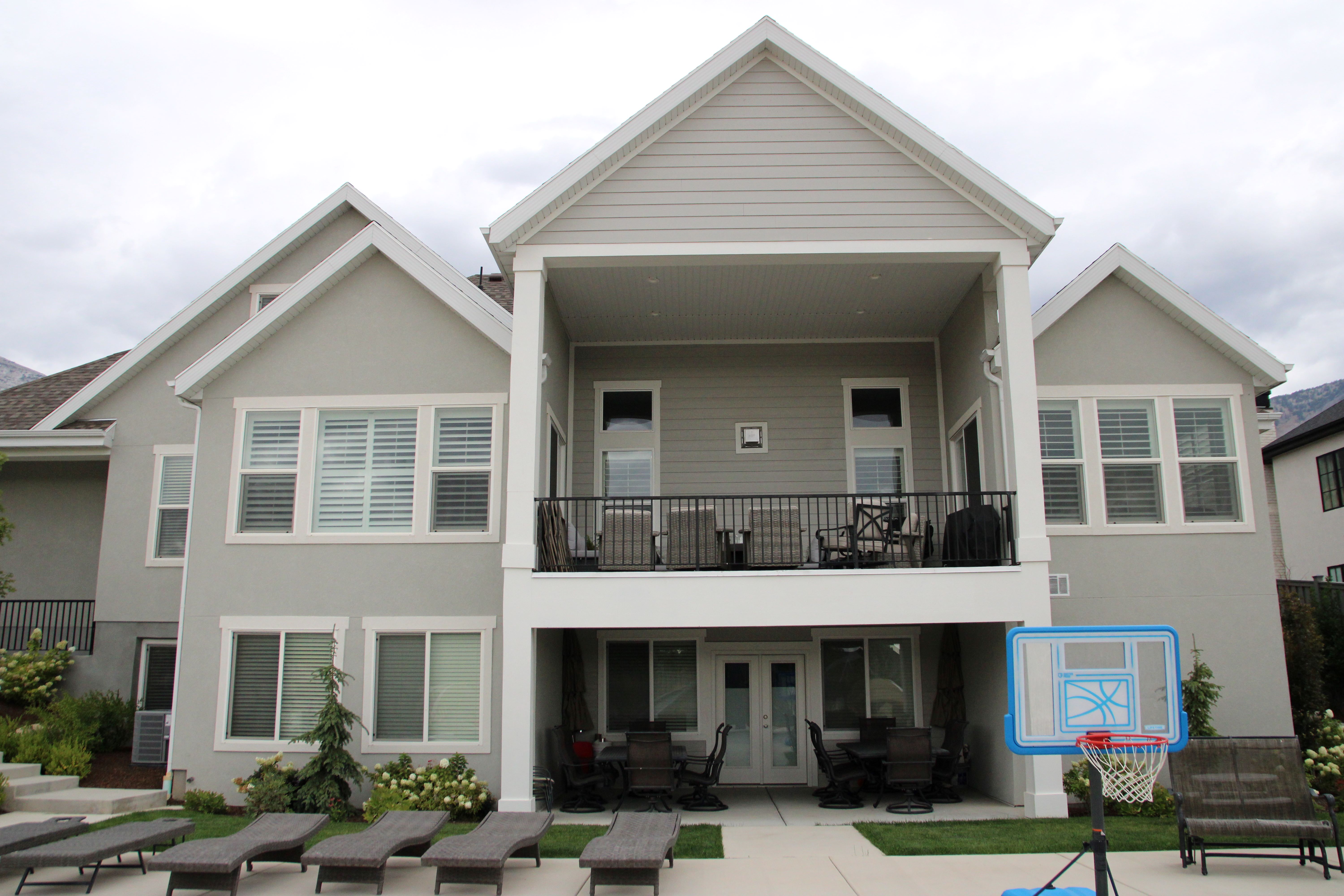 Rear exterior featuring a covered balcony, lower patio, multiple window installations, and a stucco finish