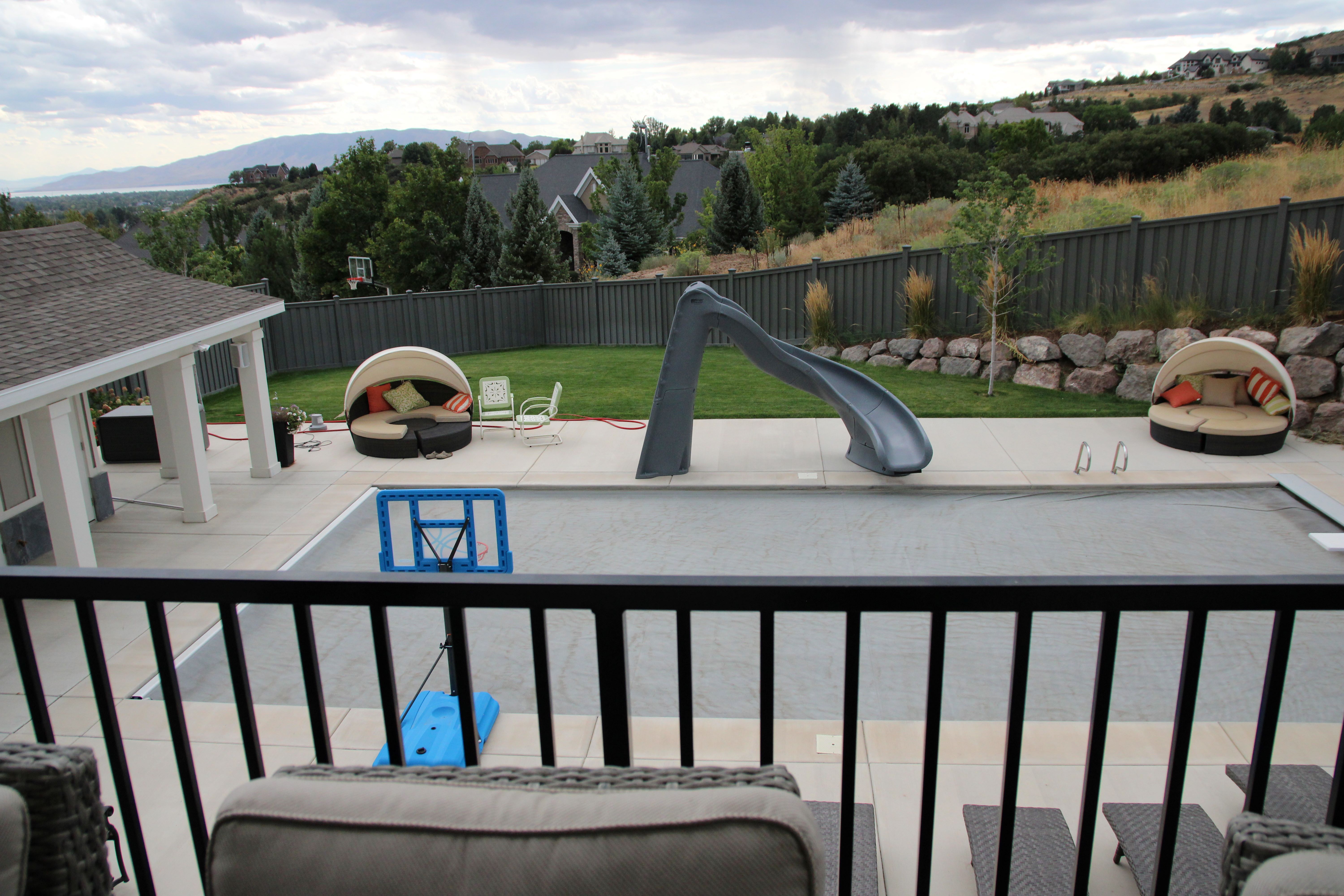 Expansive outdoor living area featuring a covered patio, concrete deck surrounding a covered swimming pool, and a sloped grass lawn