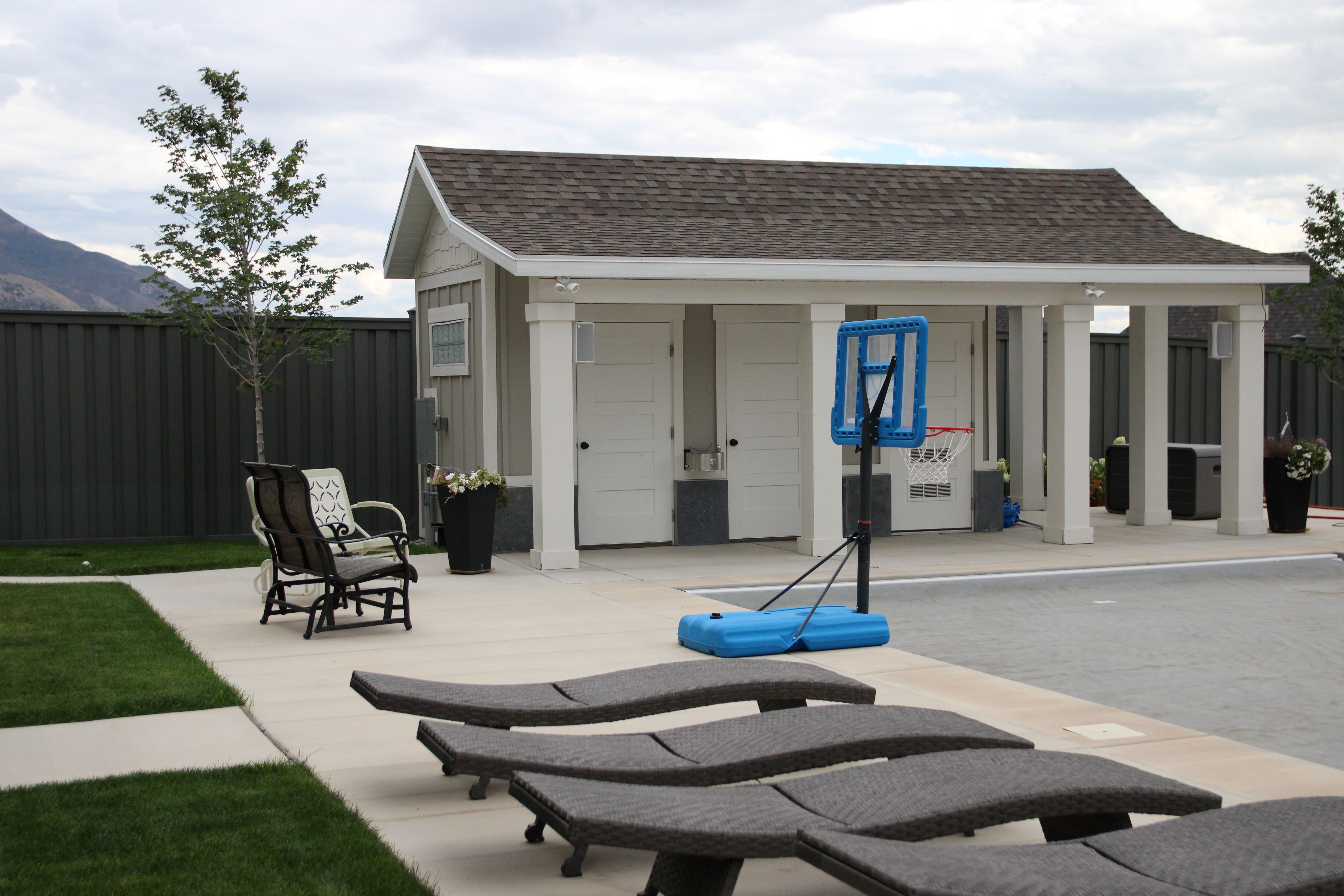 Poolside structure featuring a shingled roof, white columns, two exterior doors, and a covered patio area