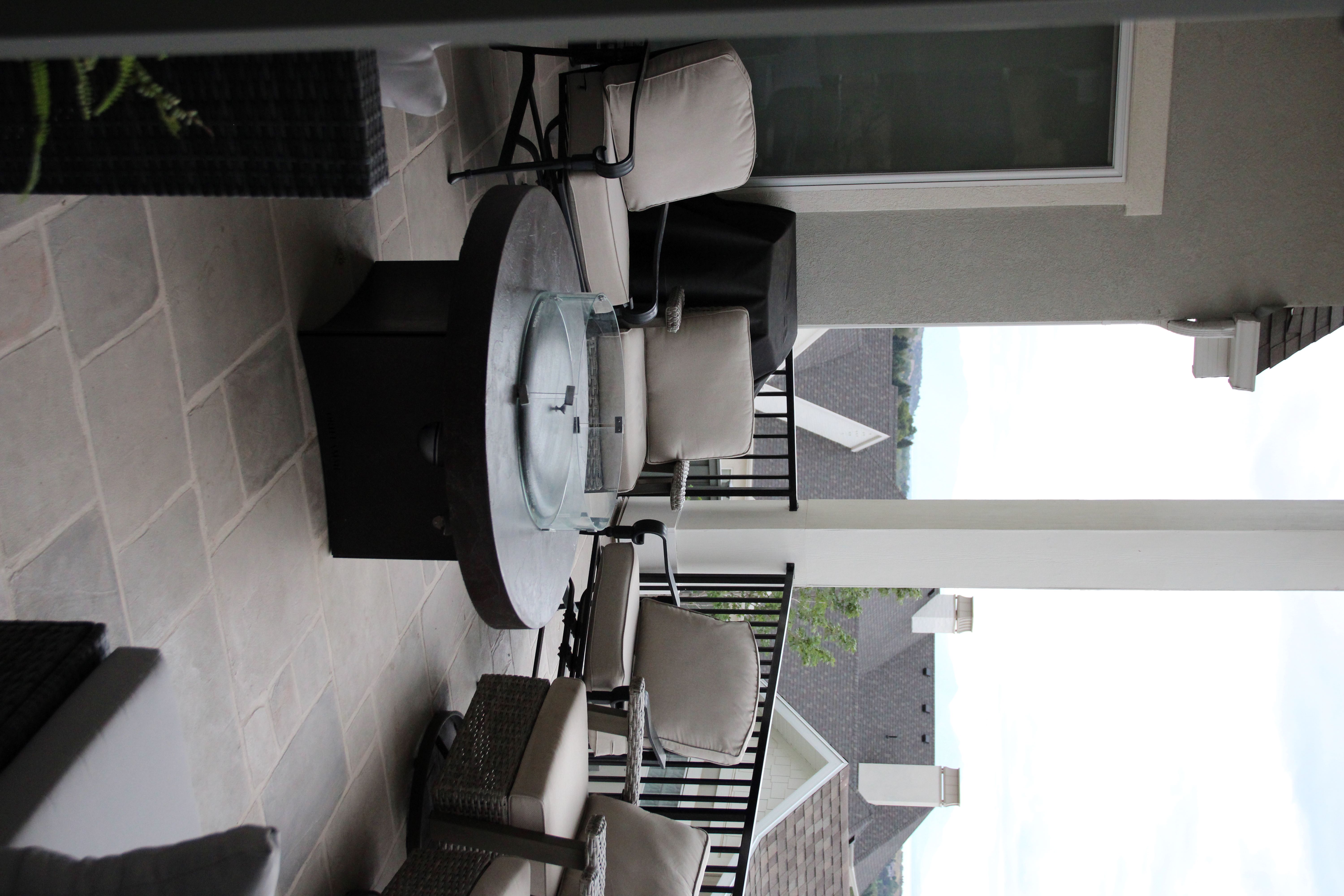 Expansive outdoor patio featuring a stone tile surface, a built-in fire pit, black metal railings, and stucco exterior