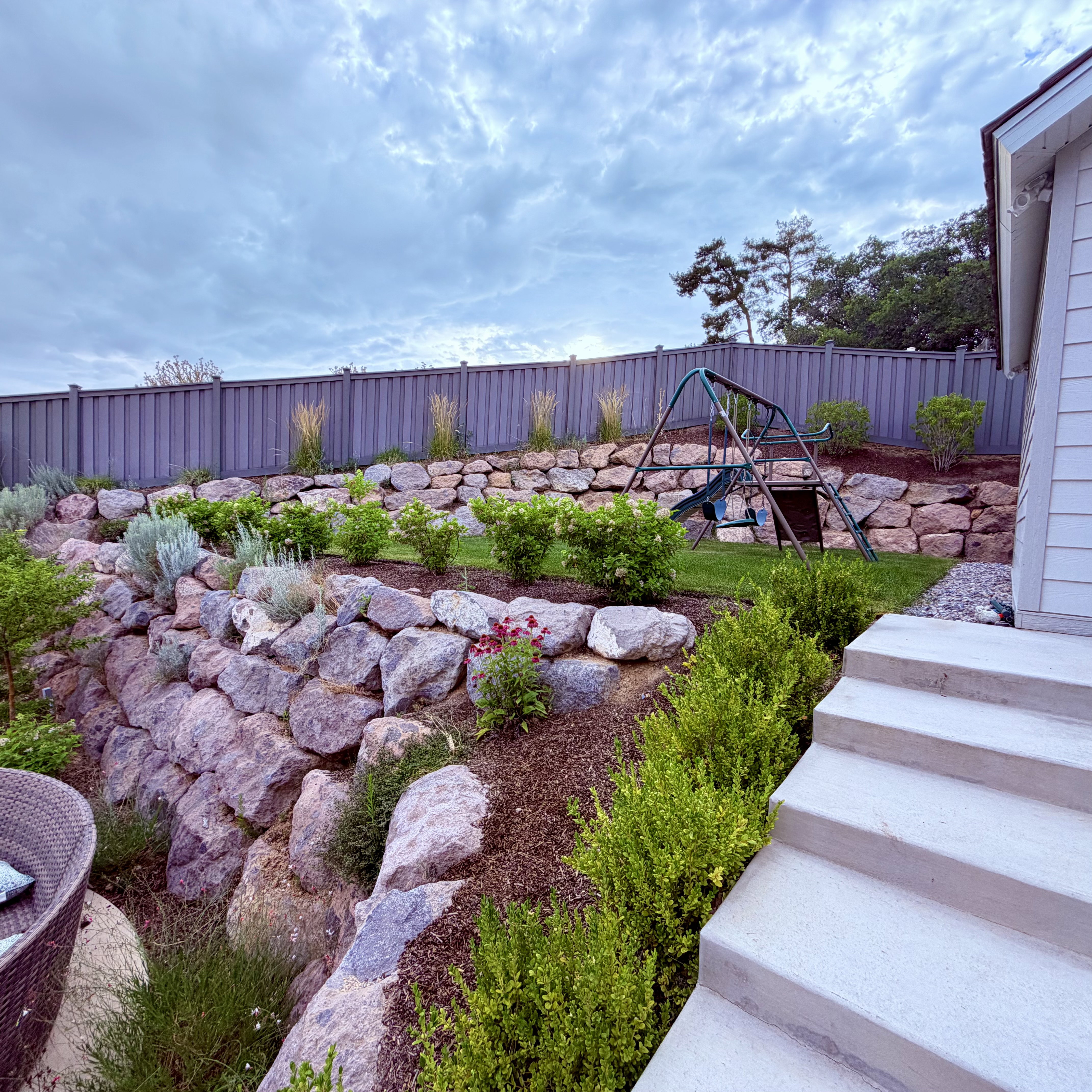 Terraced backyard featuring extensive rock retaining walls, varied shrubbery, and a manicured lawn area