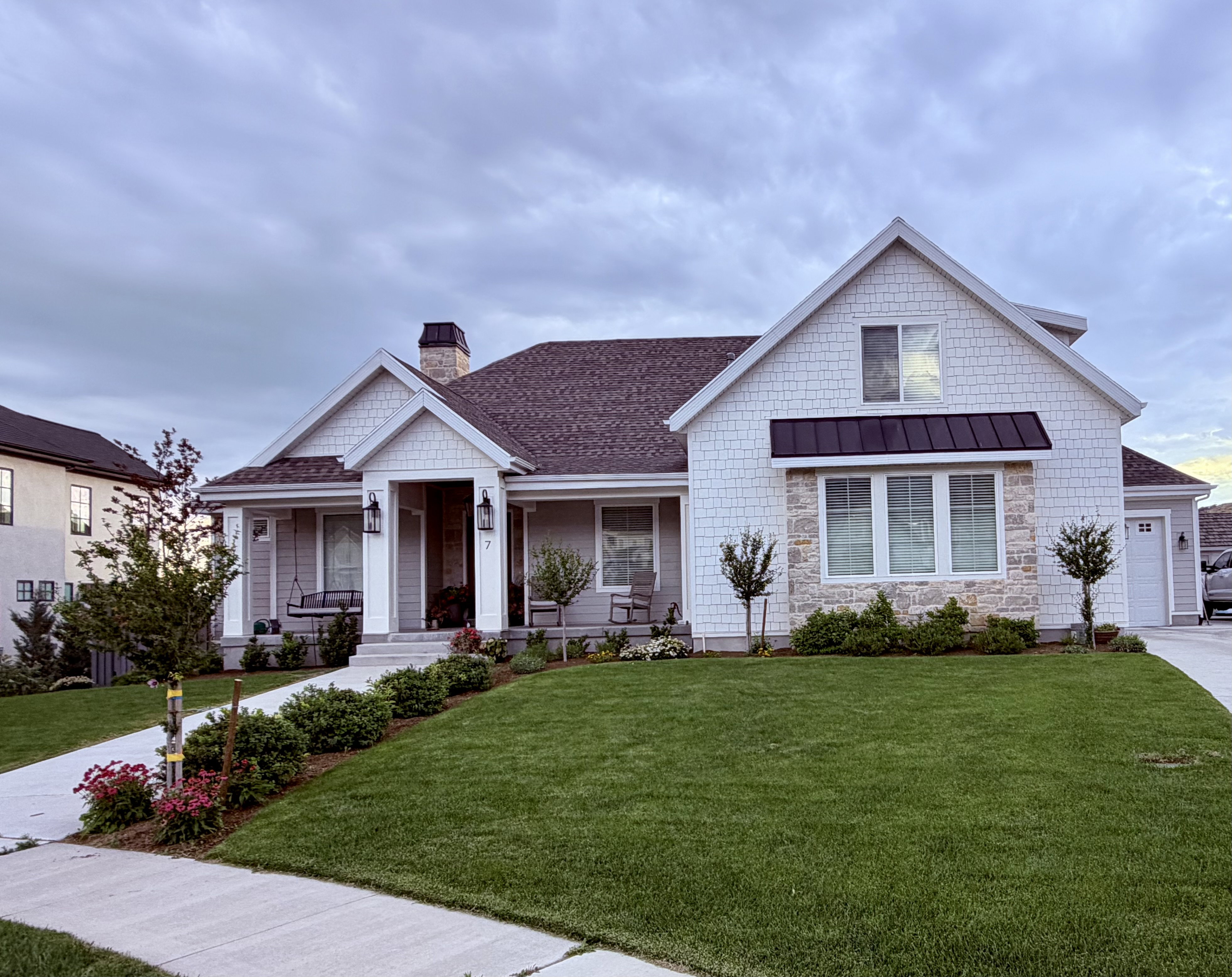 Contemporary craftsman-style residence featuring white shingle siding, a stone facade accent, a covered front porch, and a dark metal awning over the front windows