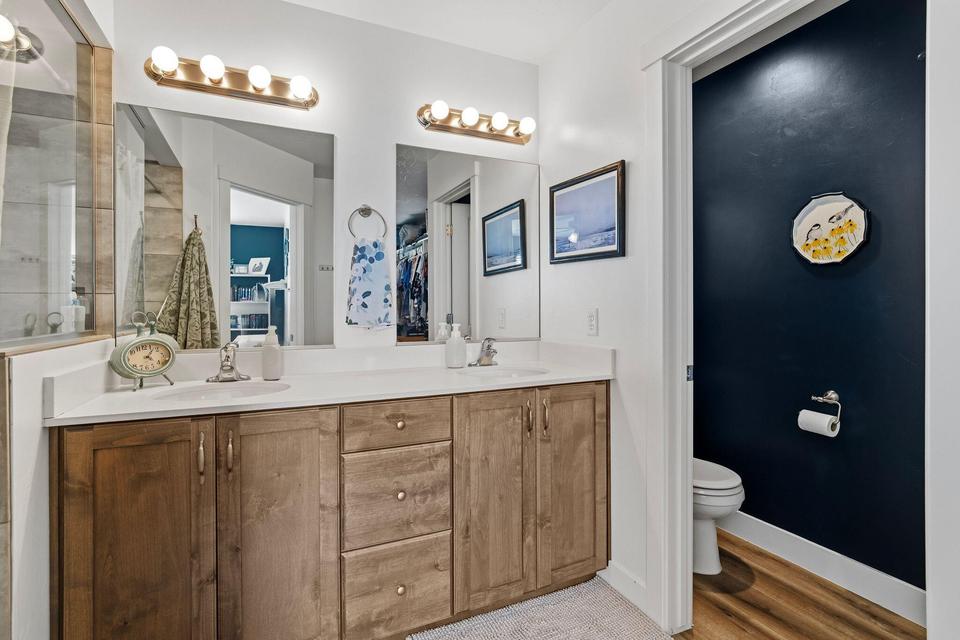 Dual vanity with wood-finish cabinetry, white countertops, and individual mirrors featuring overhead lighting