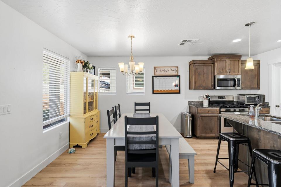 Open-concept kitchen and dining area featuring wood-finish flooring, a kitchen island with seating, dark wood cabinetry, stainless steel appliances, and a dining table with a chandelier