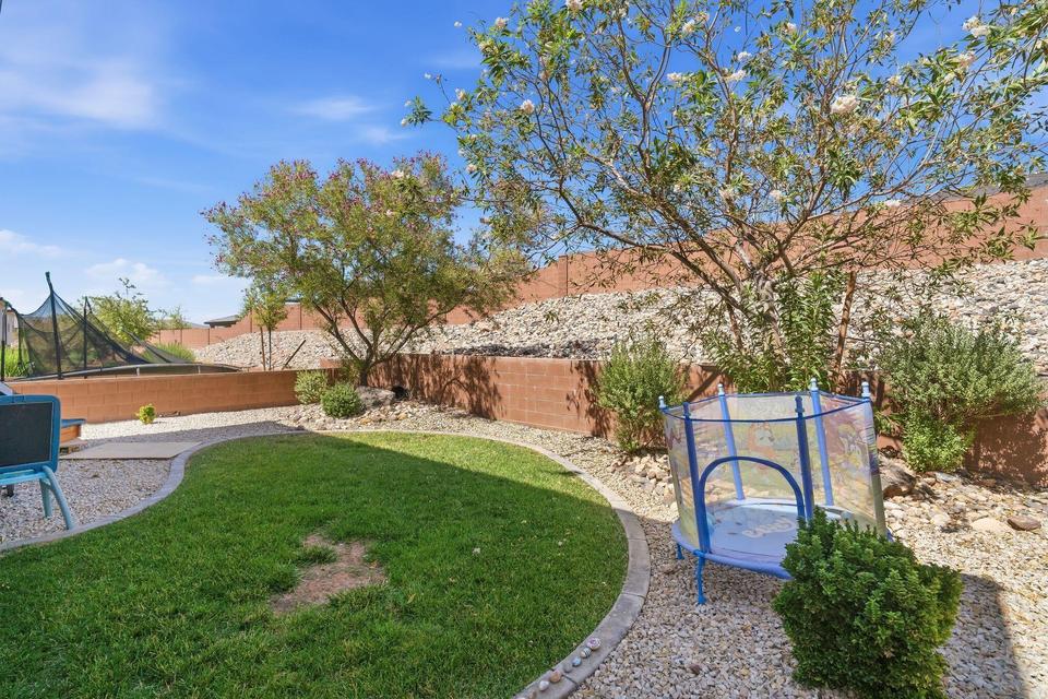 Landscaped backyard featuring a grass lawn, gravel areas, mature trees, and a retaining wall