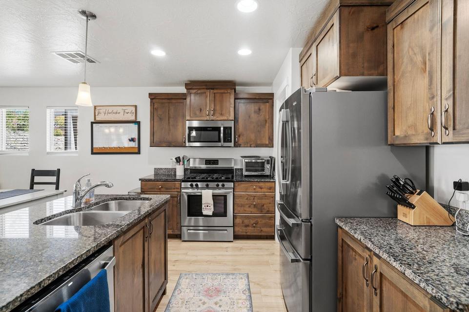 Kitchen featuring wood cabinetry, stainless steel appliances, speckled stone countertops, a double basin sink, and recessed lighting