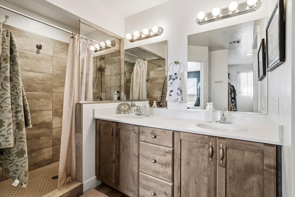 Bathroom featuring a spacious double vanity with wood-finish cabinetry and integrated sinks, complemented by two large mirrors and two overhead light fixtures