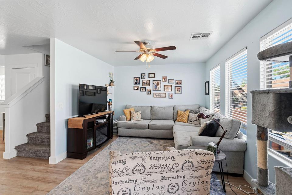 Open-concept living space with wood-finish flooring, a ceiling fan, and multiple windows with blinds