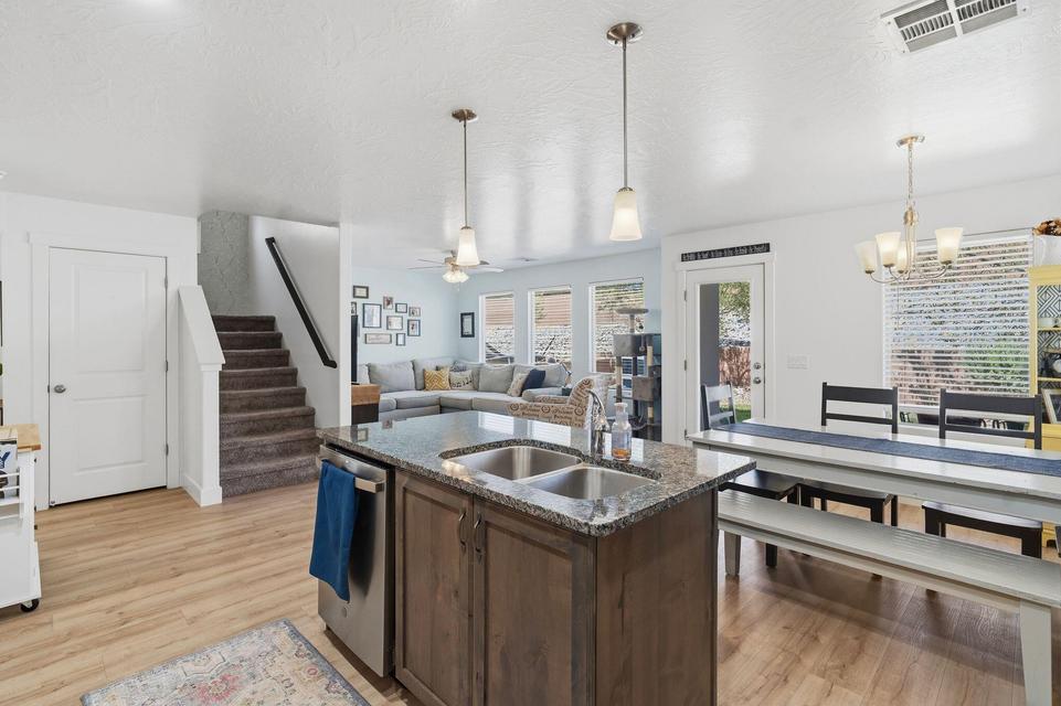 Open-concept kitchen and dining area featuring wood-finish flooring, a kitchen island with dual sinks and granite countertops, stainless steel dishwasher, and a chandelier over the dining space