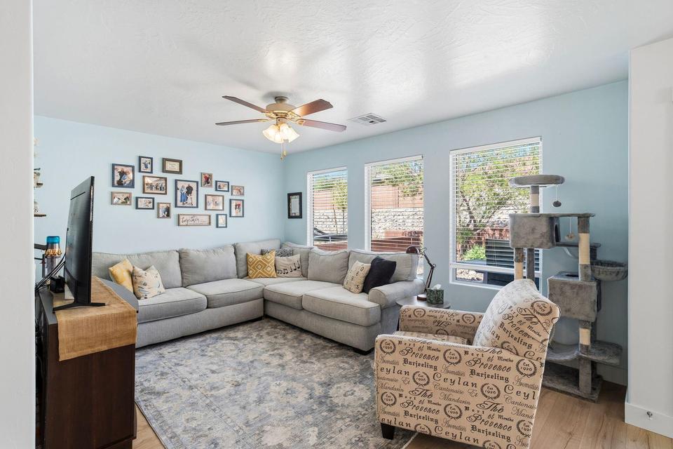 Living area featuring three large windows with horizontal blinds, a ceiling fan with integrated lighting, and wood-finish flooring