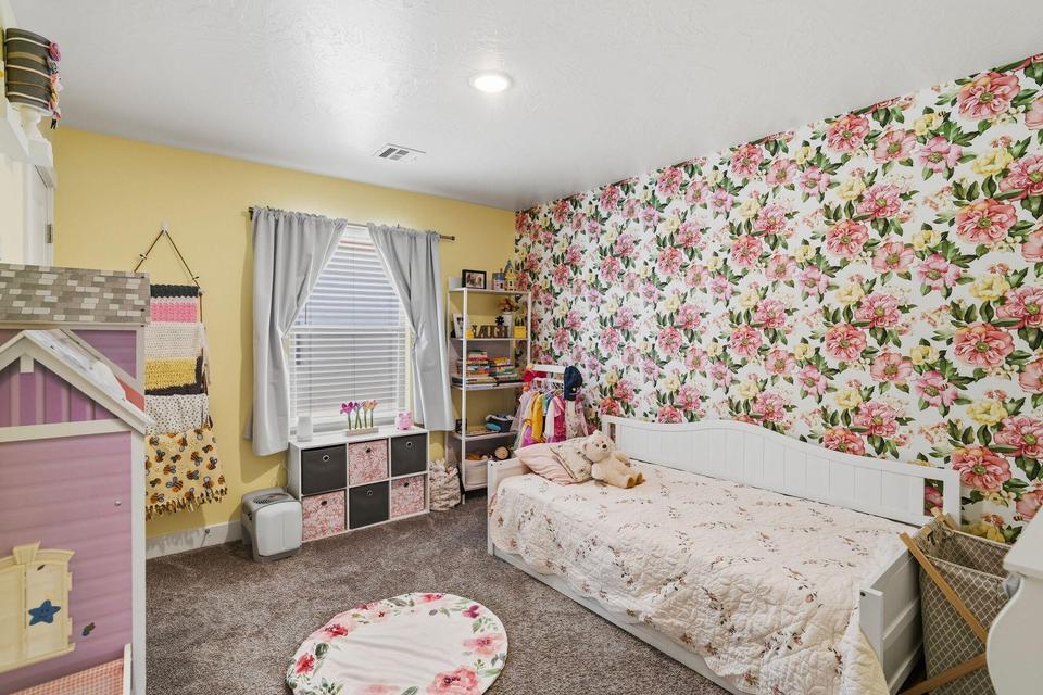 Spacious room featuring a floral accent wall, plush carpeting, and a large window with blinds