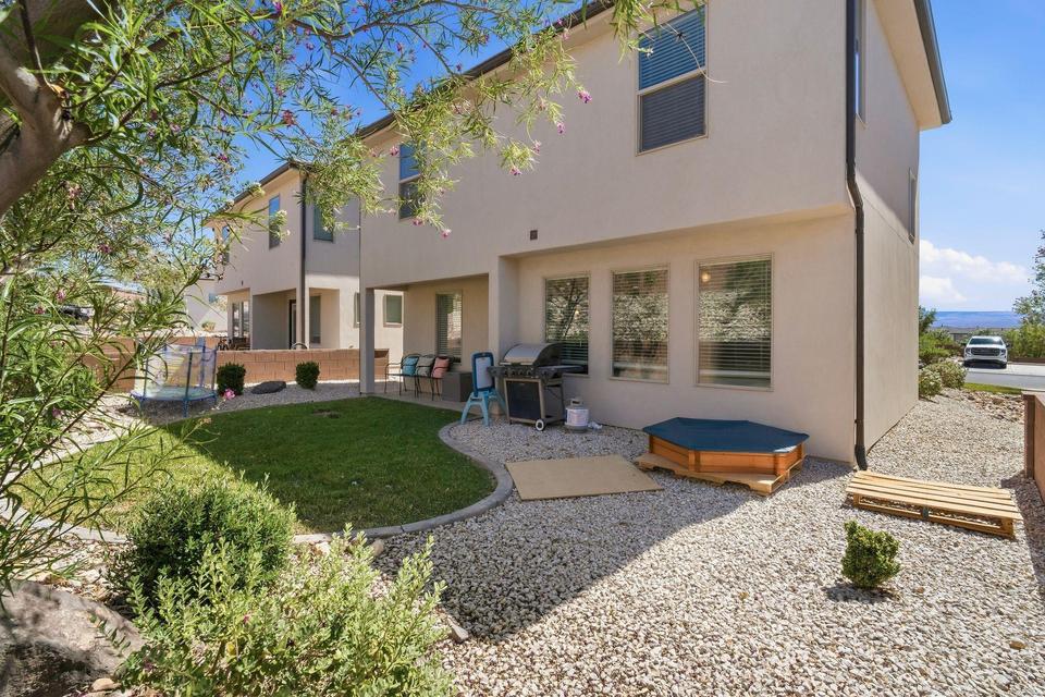 Rear exterior featuring stucco finish, multiple windows with blinds, a covered patio area, and a combination of manicured lawn and gravel landscaping