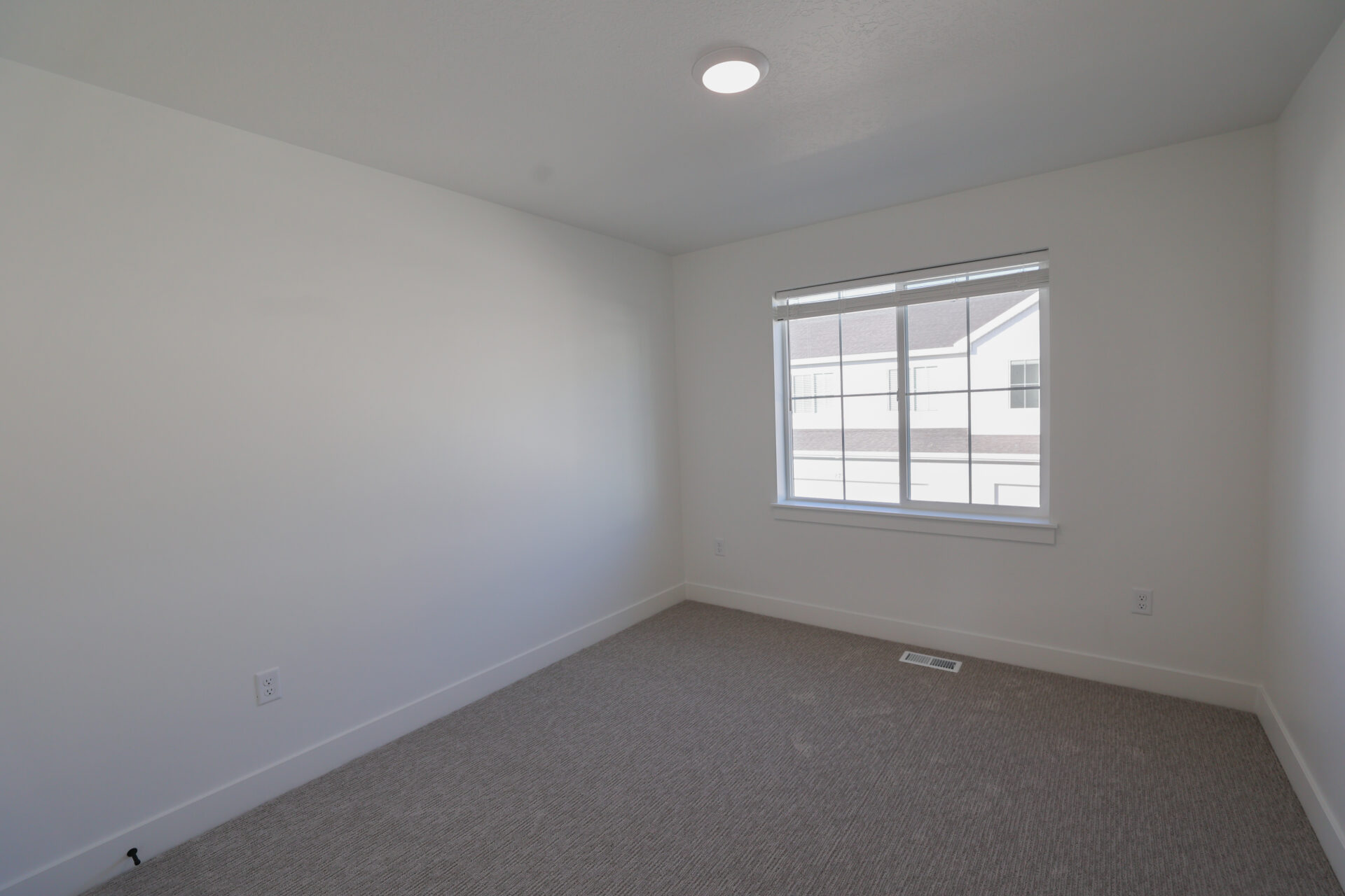 Neutral tone bedroom with a large window, recessed lighting, and grey patterned carpeting