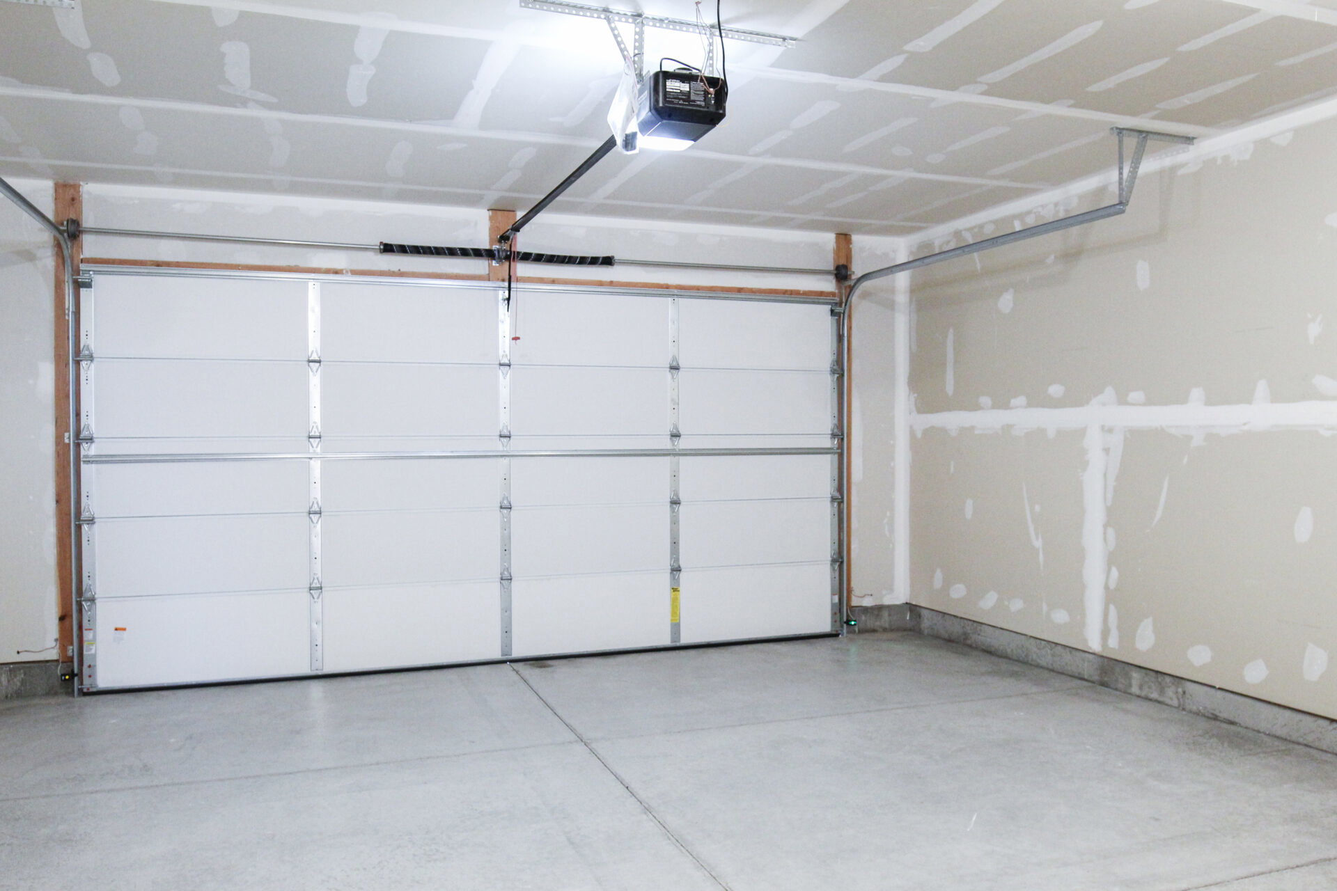 Garage interior featuring a sectional white garage door, overhead garage door opener, concrete flooring, and unfinished drywall walls