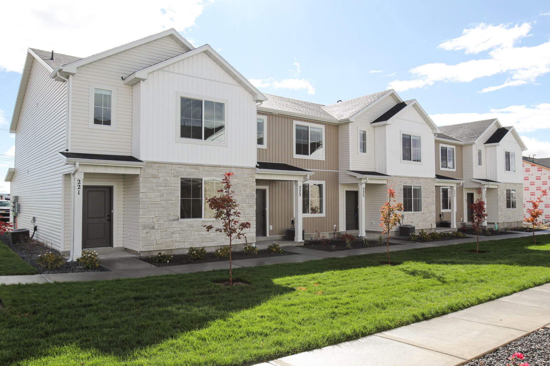 Contemporary townhome-style residences featuring varied neutral siding, stone veneer accents, and dark trim elements