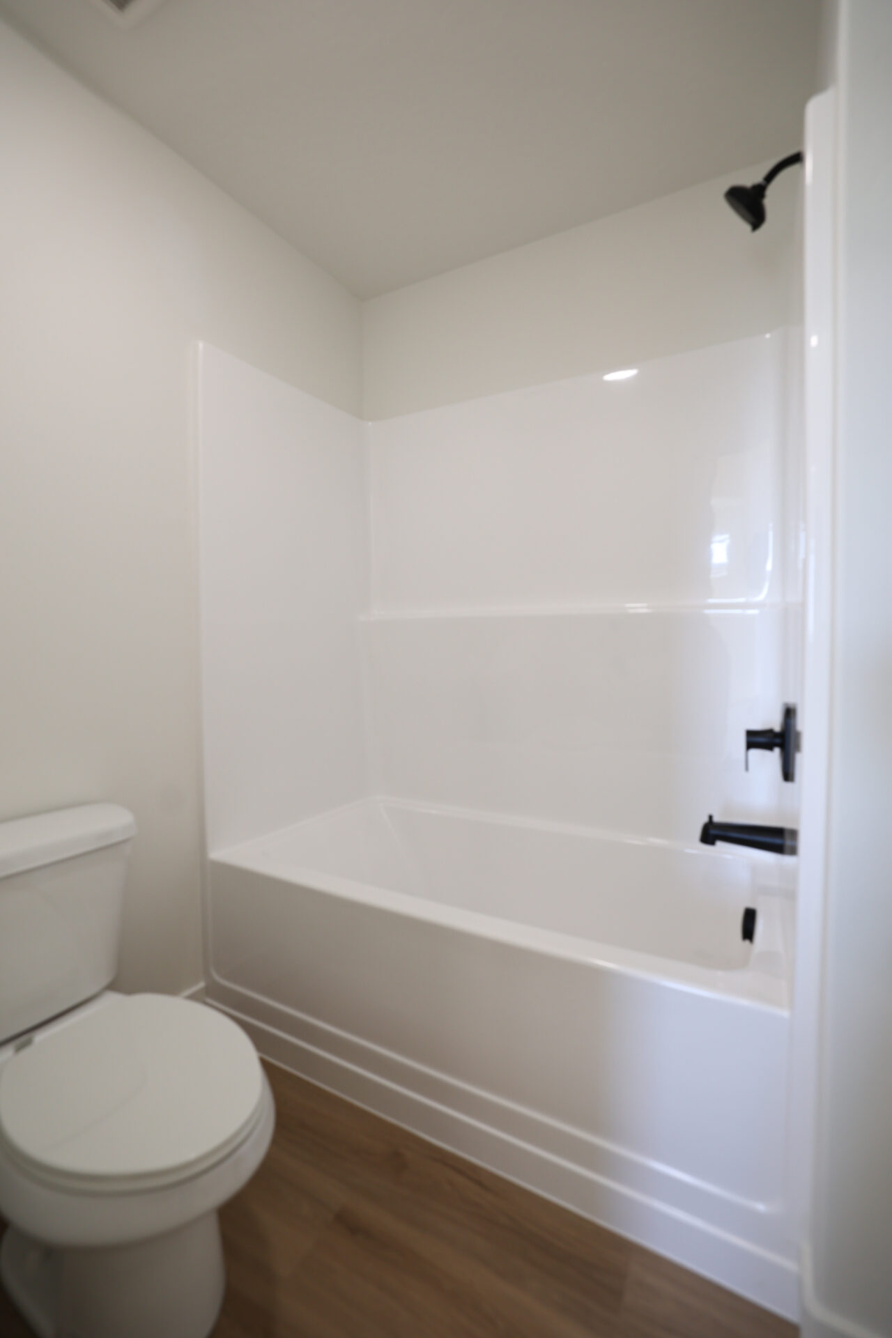 White bathtub with integrated shower, accented by matte black fixtures, set against wood-finish flooring