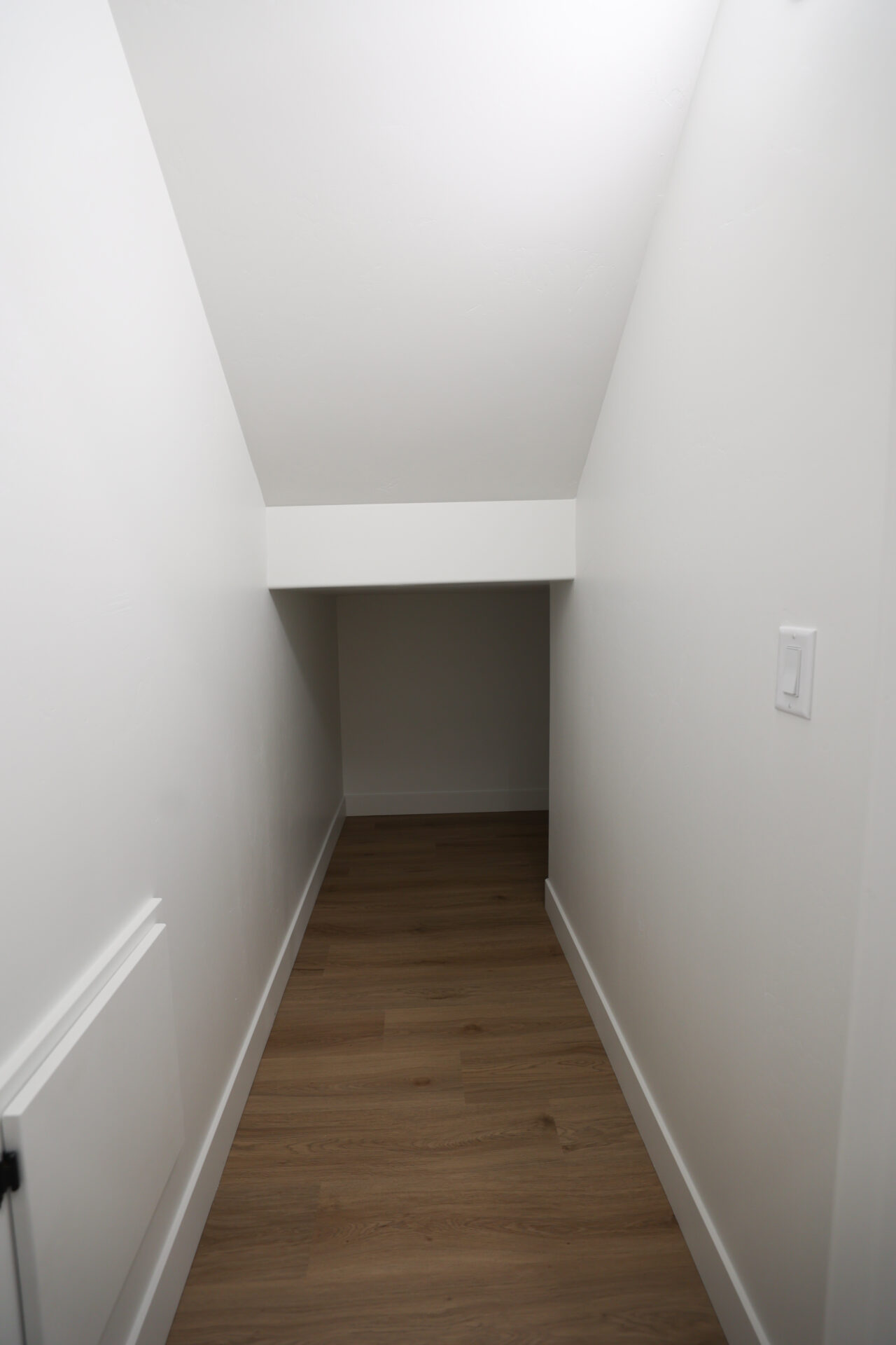 Under-stair storage area featuring wood-finish flooring, white baseboards, and bright white walls