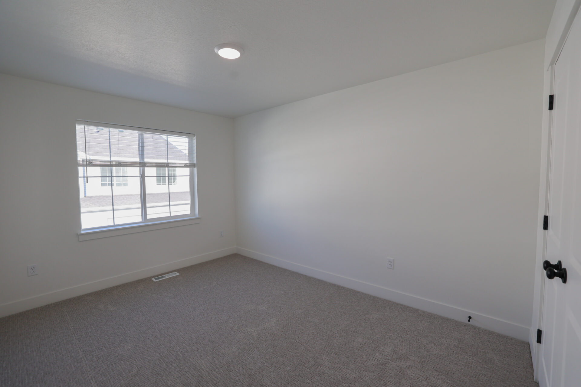 Bedroom featuring neutral-toned carpeting, white walls, and a large window with white blinds