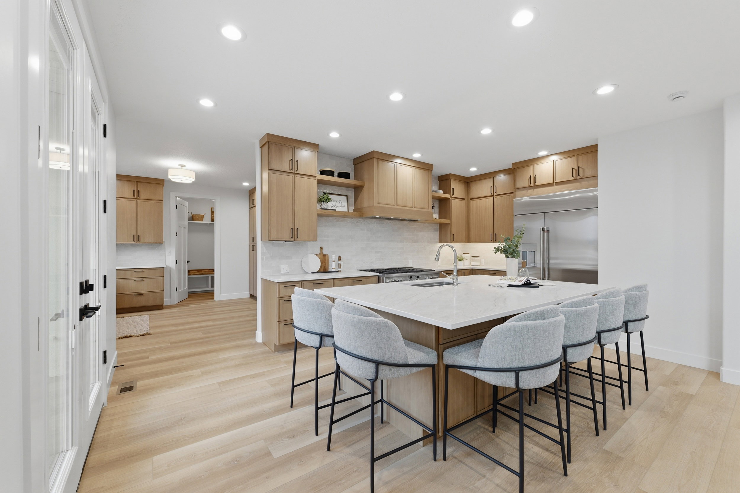 Expansive kitchen featuring light wood-finish cabinetry, a large center island with seating, stainless steel appliances, white countertops, and light wood-finish flooring