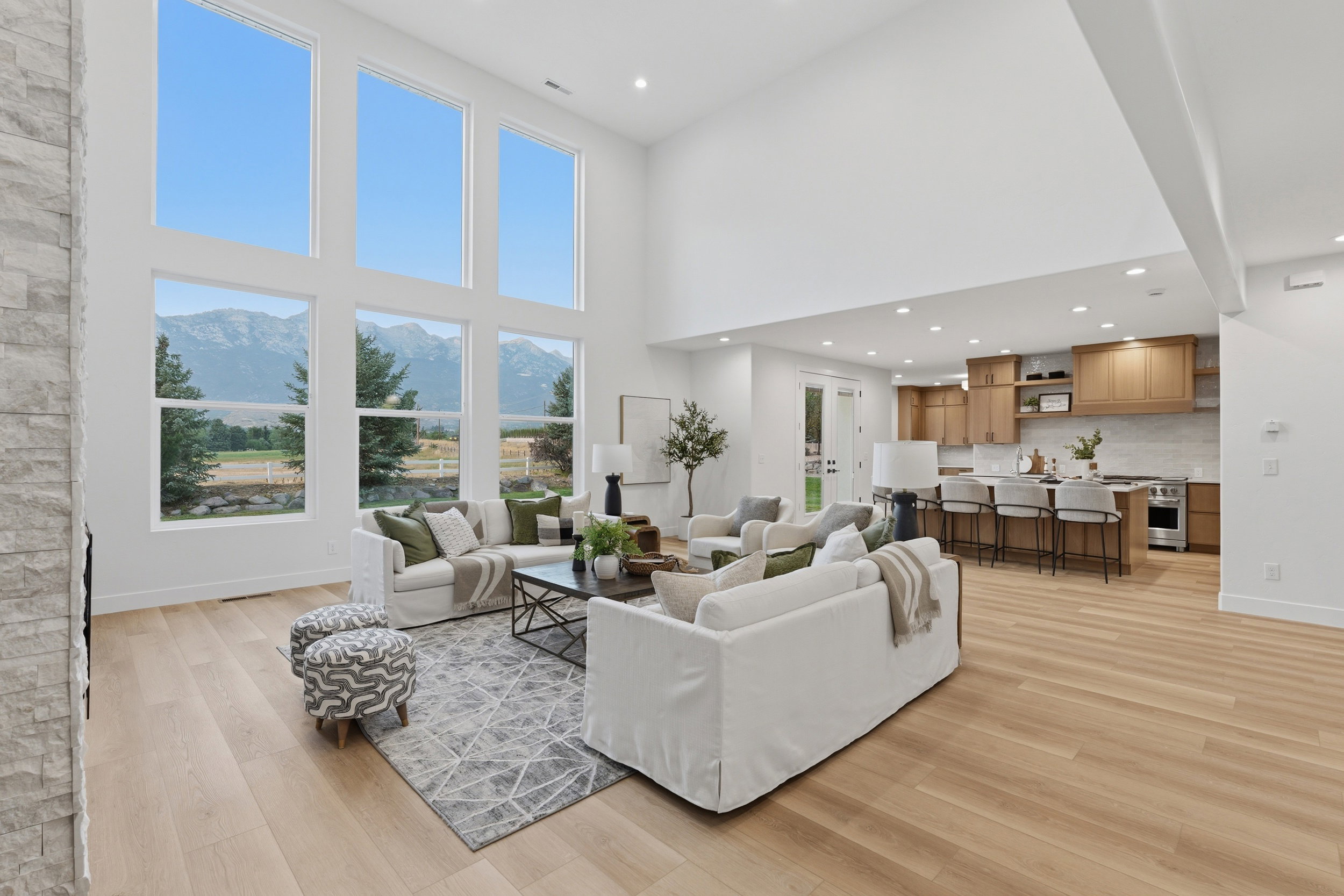 Vaulted great room featuring tall windows with mountain scenery, light wood-finish flooring, and a stone-clad fireplace