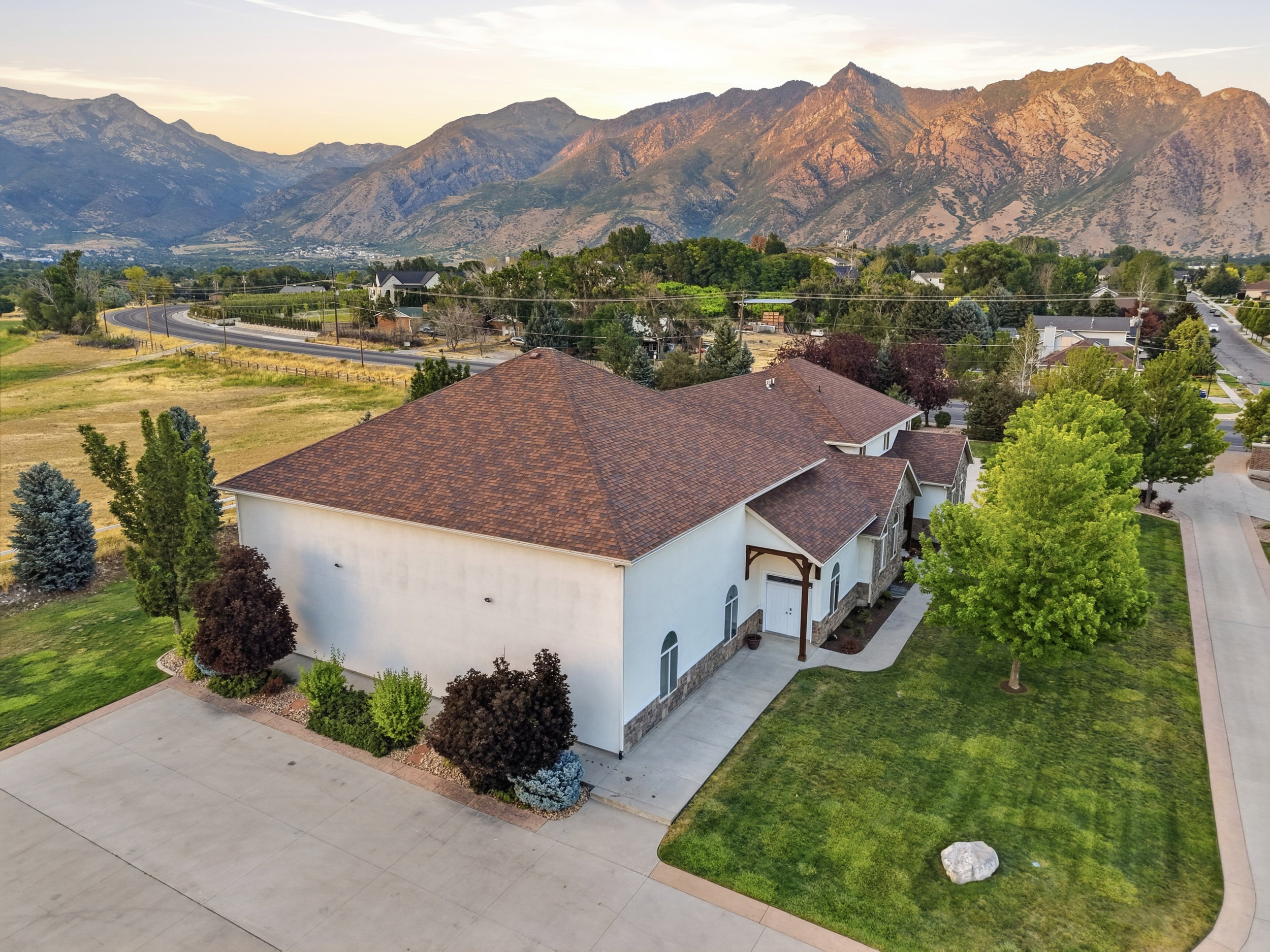 Expansive property featuring a large concrete driveway, mature landscaping, and a brown shingle roof