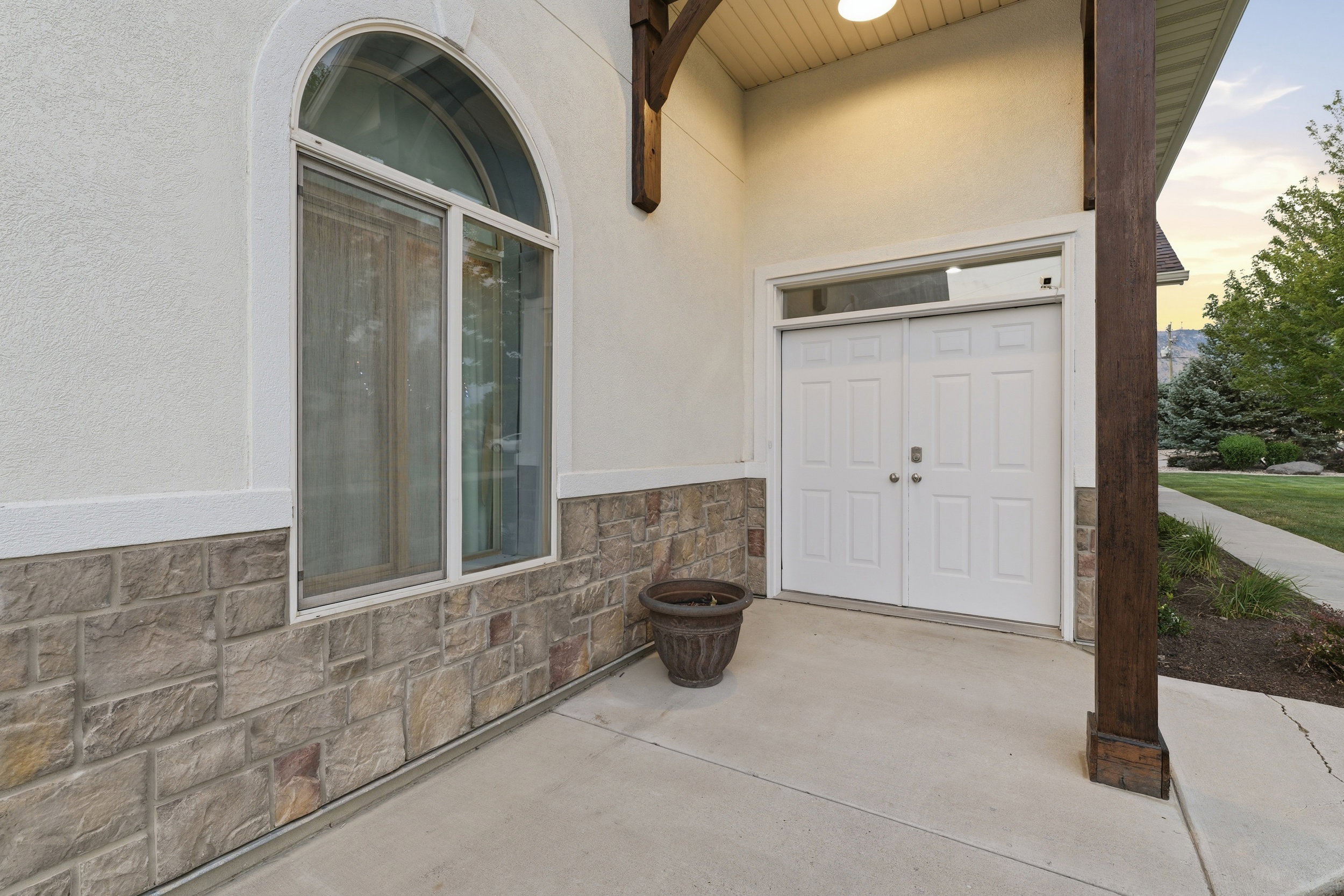Entryway featuring a double door with transom window, arched window, stone veneer siding, and stucco finish