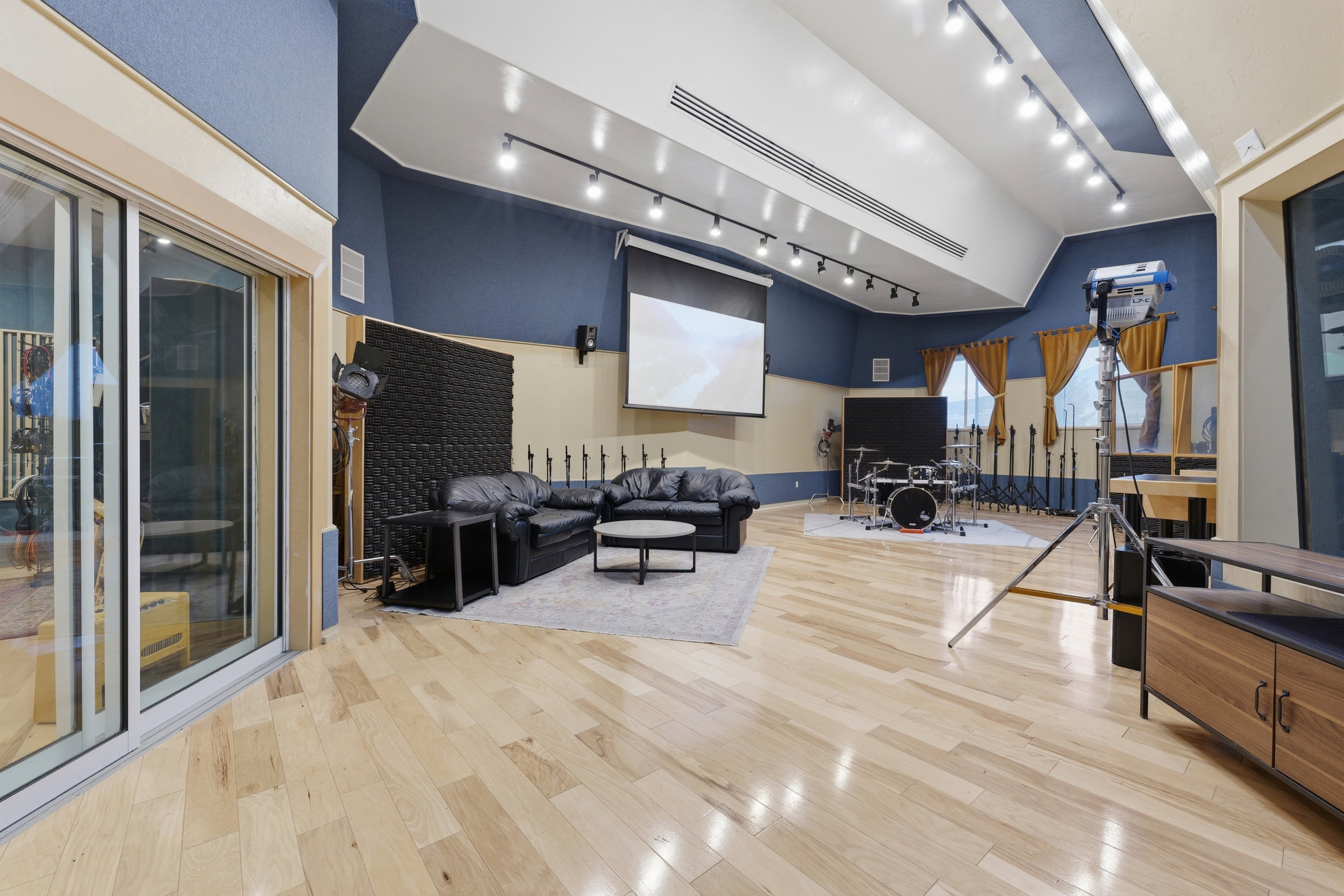 Spacious room featuring light wood-finish flooring, a vaulted ceiling with track lighting, and a projection screen