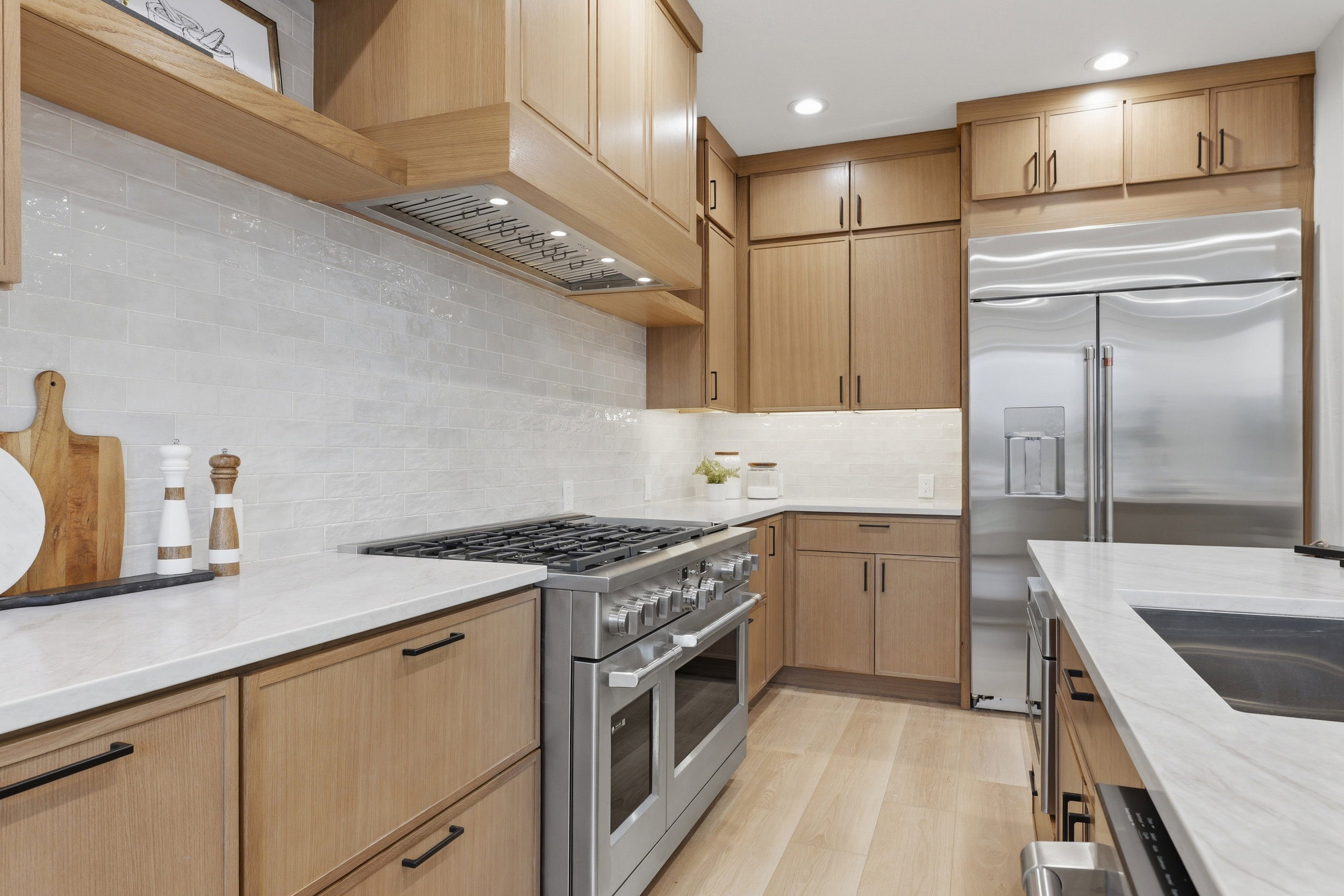Gourmet kitchen with light wood-finish cabinetry, stainless steel appliances, white subway tile backsplash, white countertops, and wood-finish flooring
