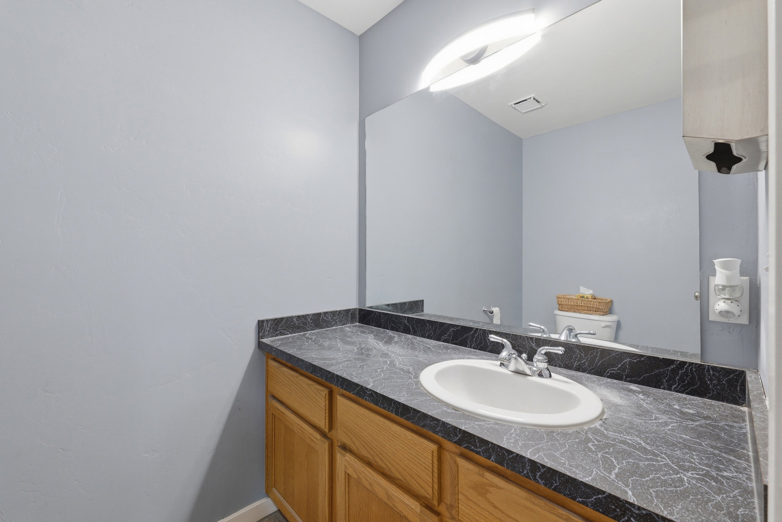 Vanity with light wood-finish cabinetry, a black patterned countertop, and an integrated white oval sink with chrome fixtures