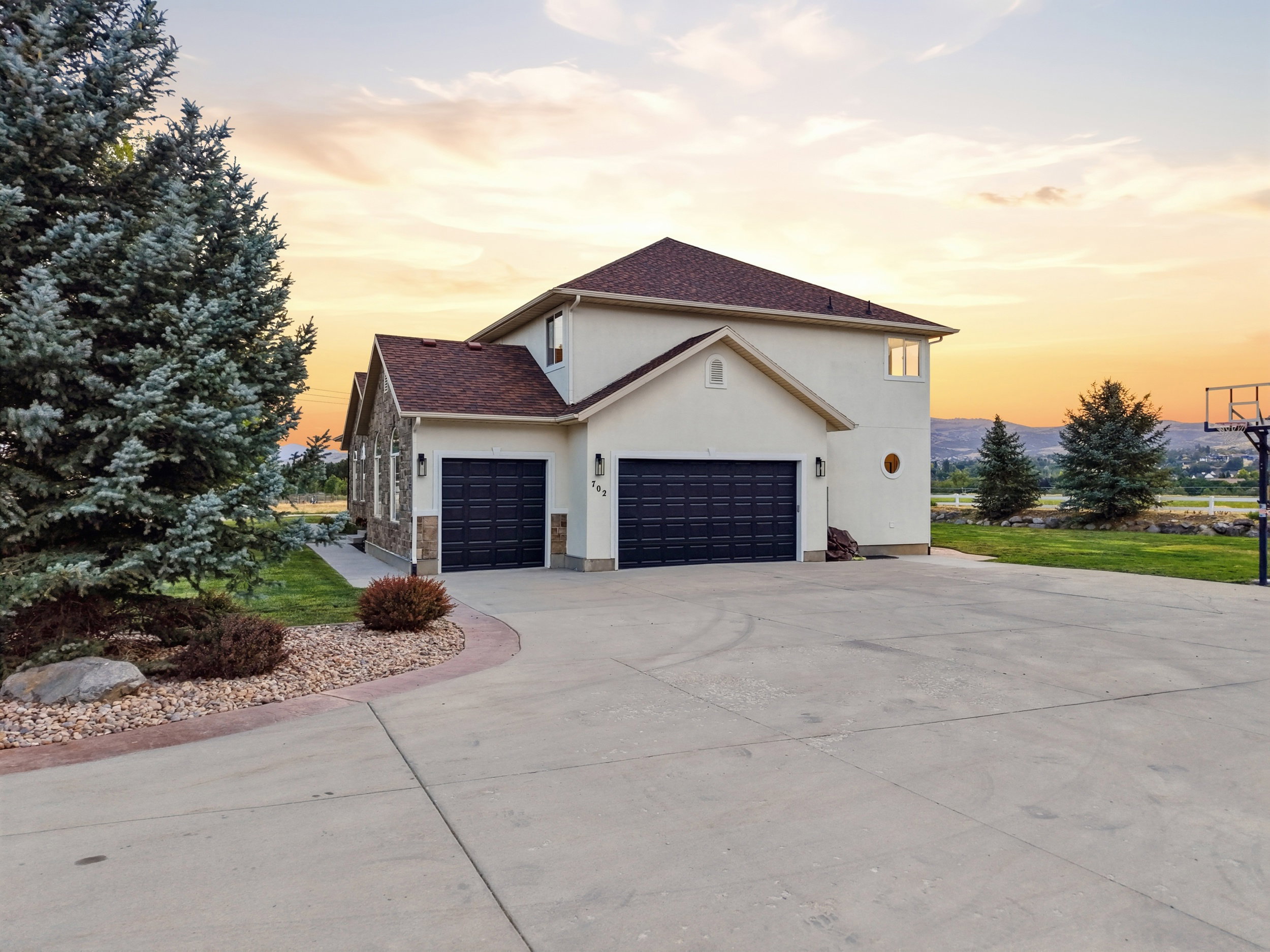Exterior featuring a stucco finish with stone accents, a multi-car garage with dark paneled doors, and mature evergreen landscaping