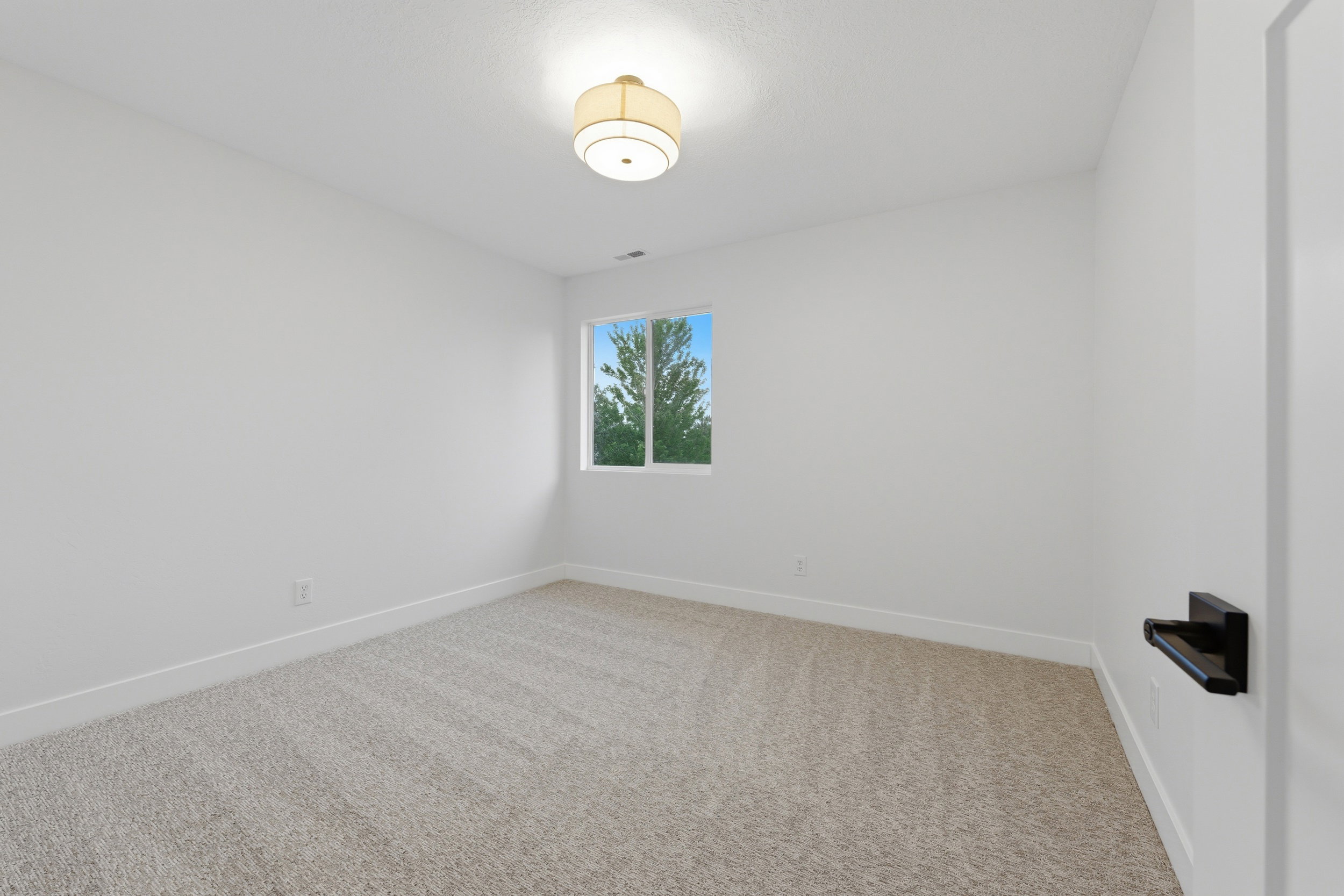 Bright room featuring light neutral carpeting, white walls, a single window, and a flush mount ceiling light fixture