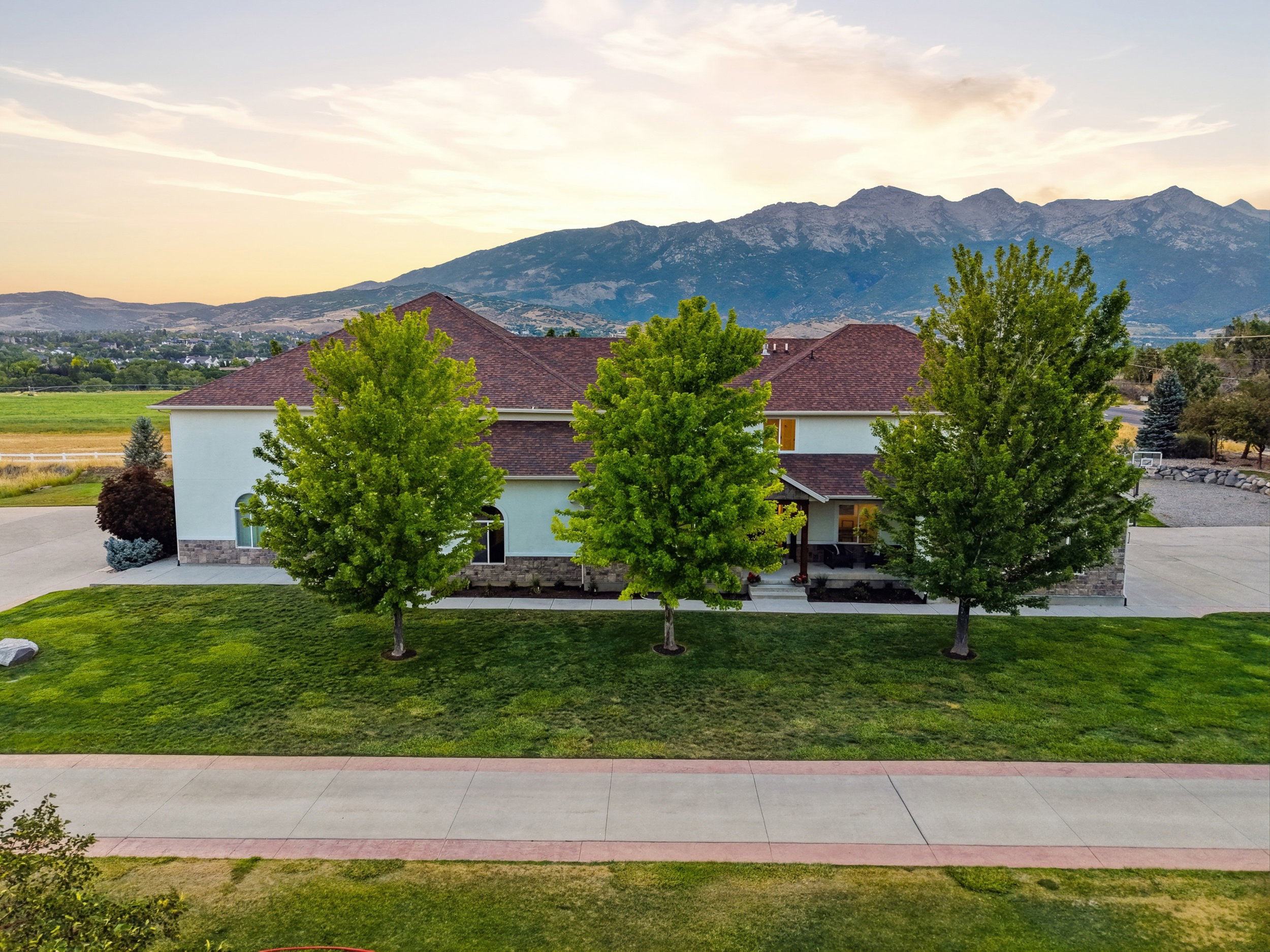 Expansive residence featuring a stucco and stone facade, a rich red-brown shingle roof, and a verdant lawn