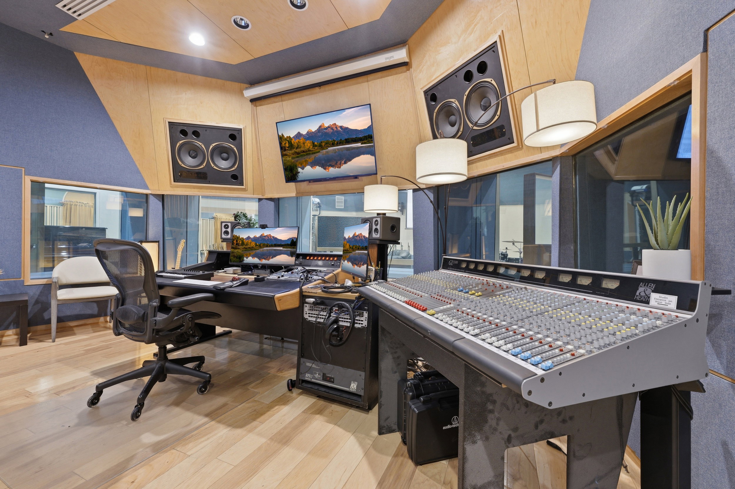 Professional-grade recording studio featuring wood-finish flooring, acoustic wall paneling, integrated audio equipment, large format mixing console, and soundproof windows