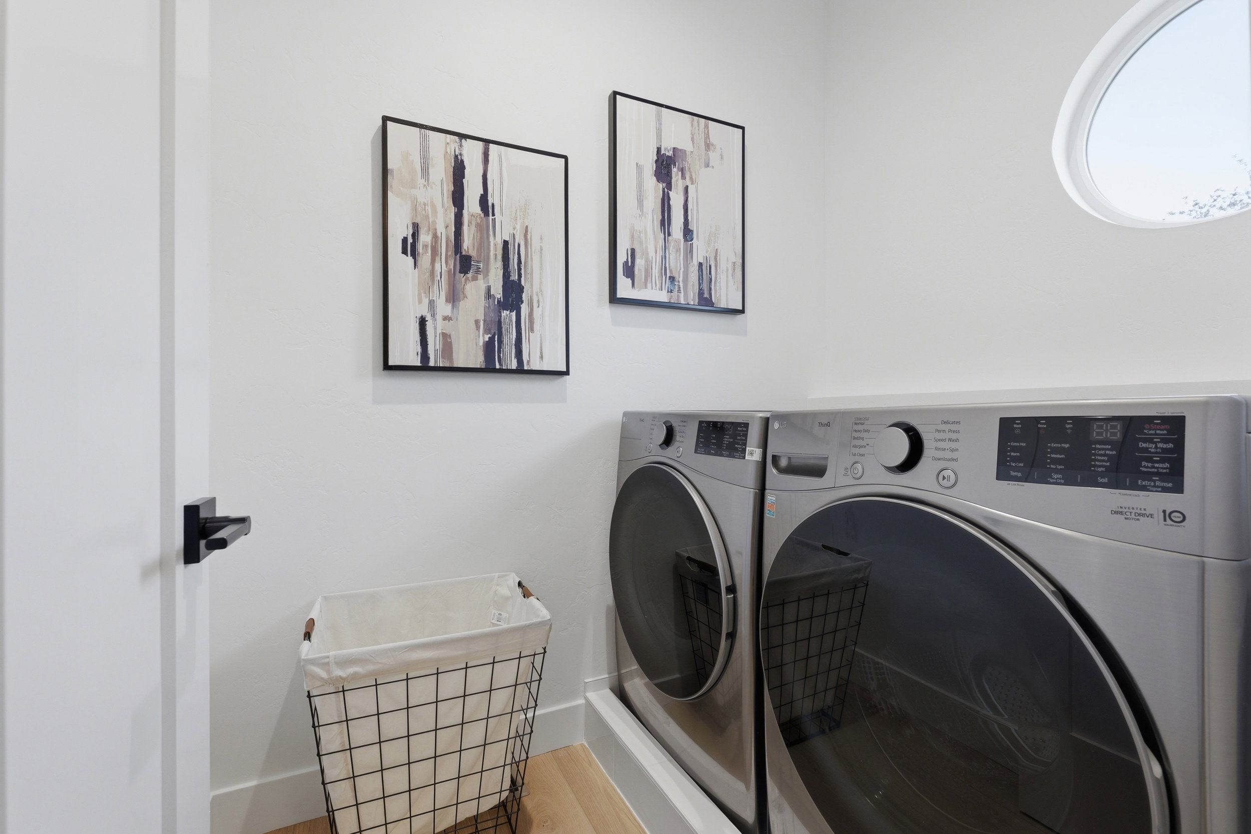 Laundry area featuring a circular window, white walls, and wood-finish flooring