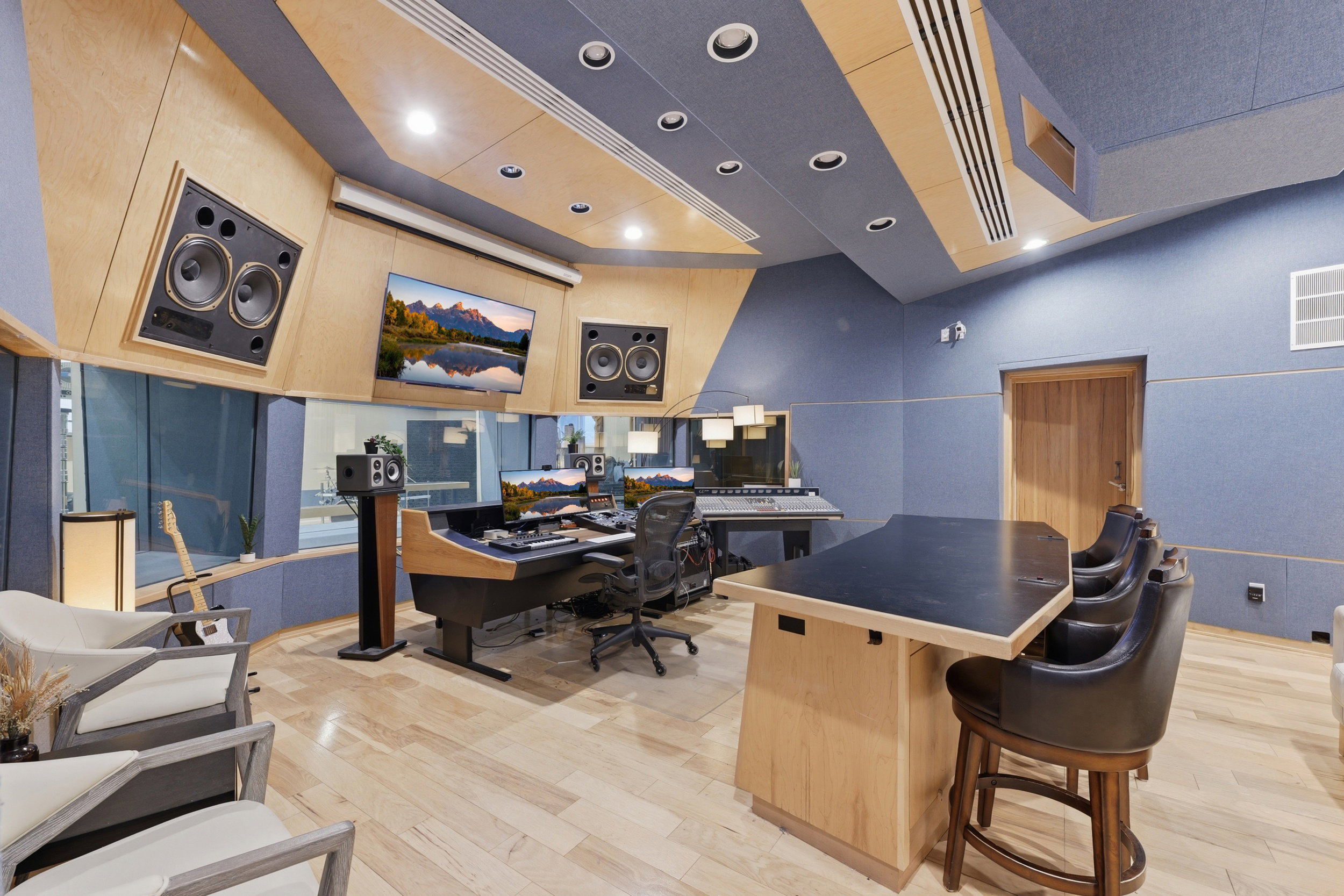 Professional sound recording studio featuring acoustic wall and ceiling paneling, recessed lighting, wood-finish flooring, and a built-in workstation