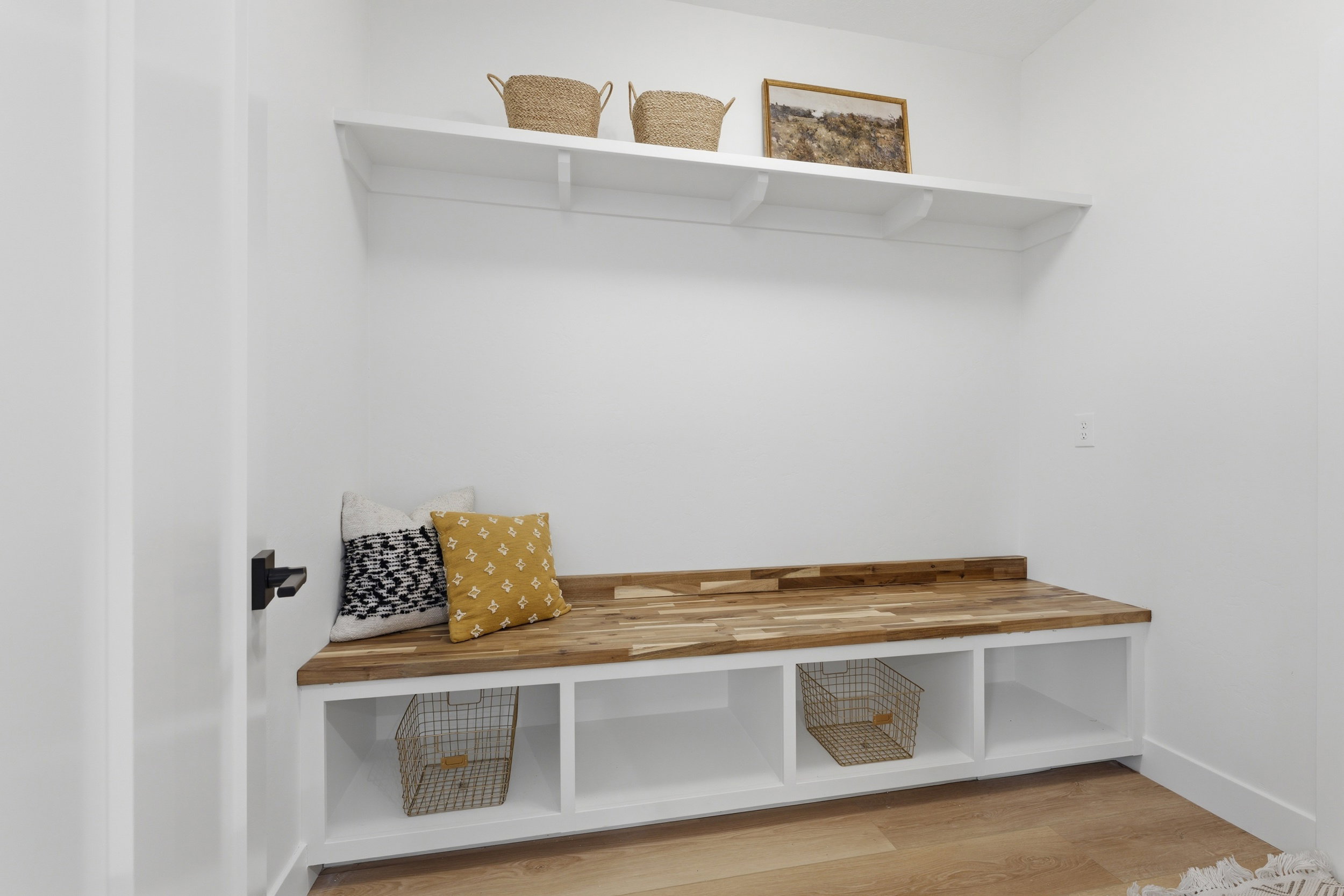 Built-in entryway bench with a wood-finish top and white cabinetry featuring open storage compartments