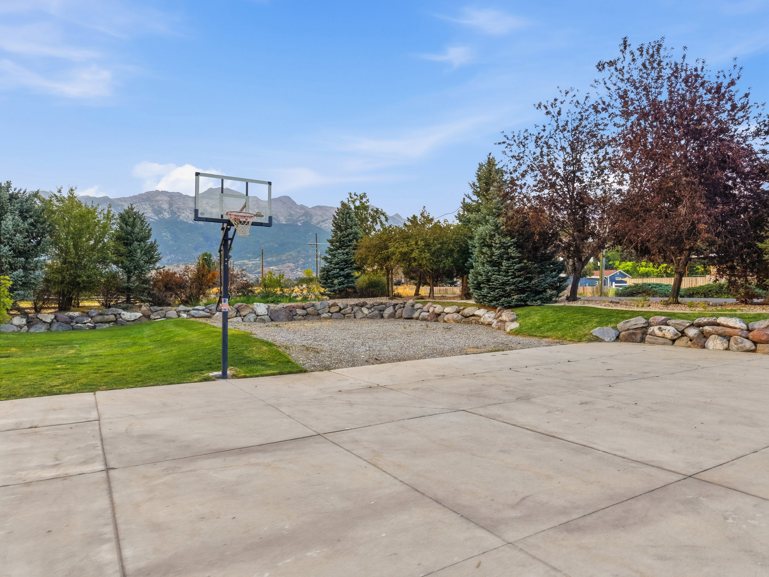 Expansive concrete paved area with a basketball hoop, surrounded by manicured lawns and mature trees