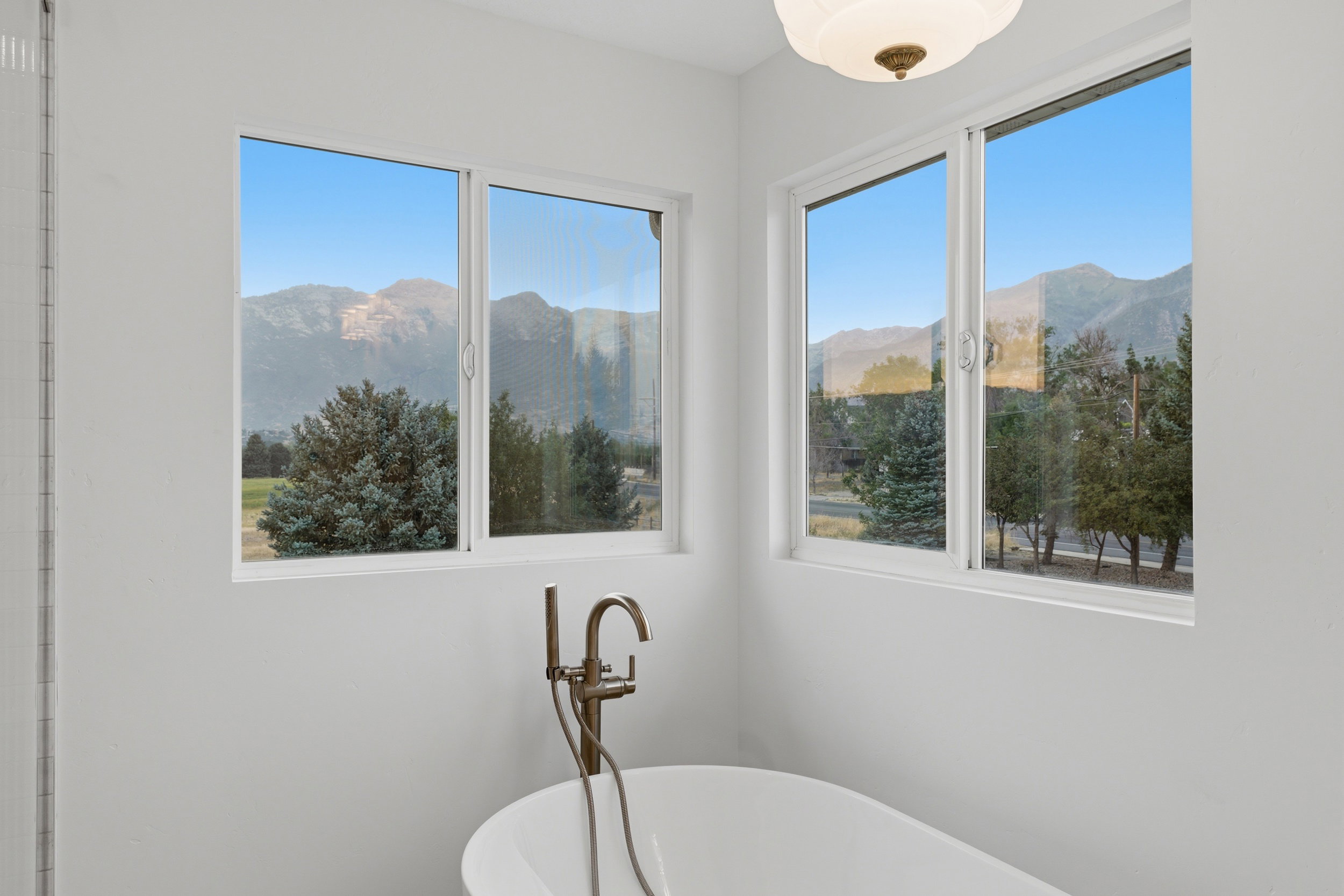 Freestanding soaking tub with a floor-mounted bronze-finish faucet, positioned below two large windows with mountain and tree scenery