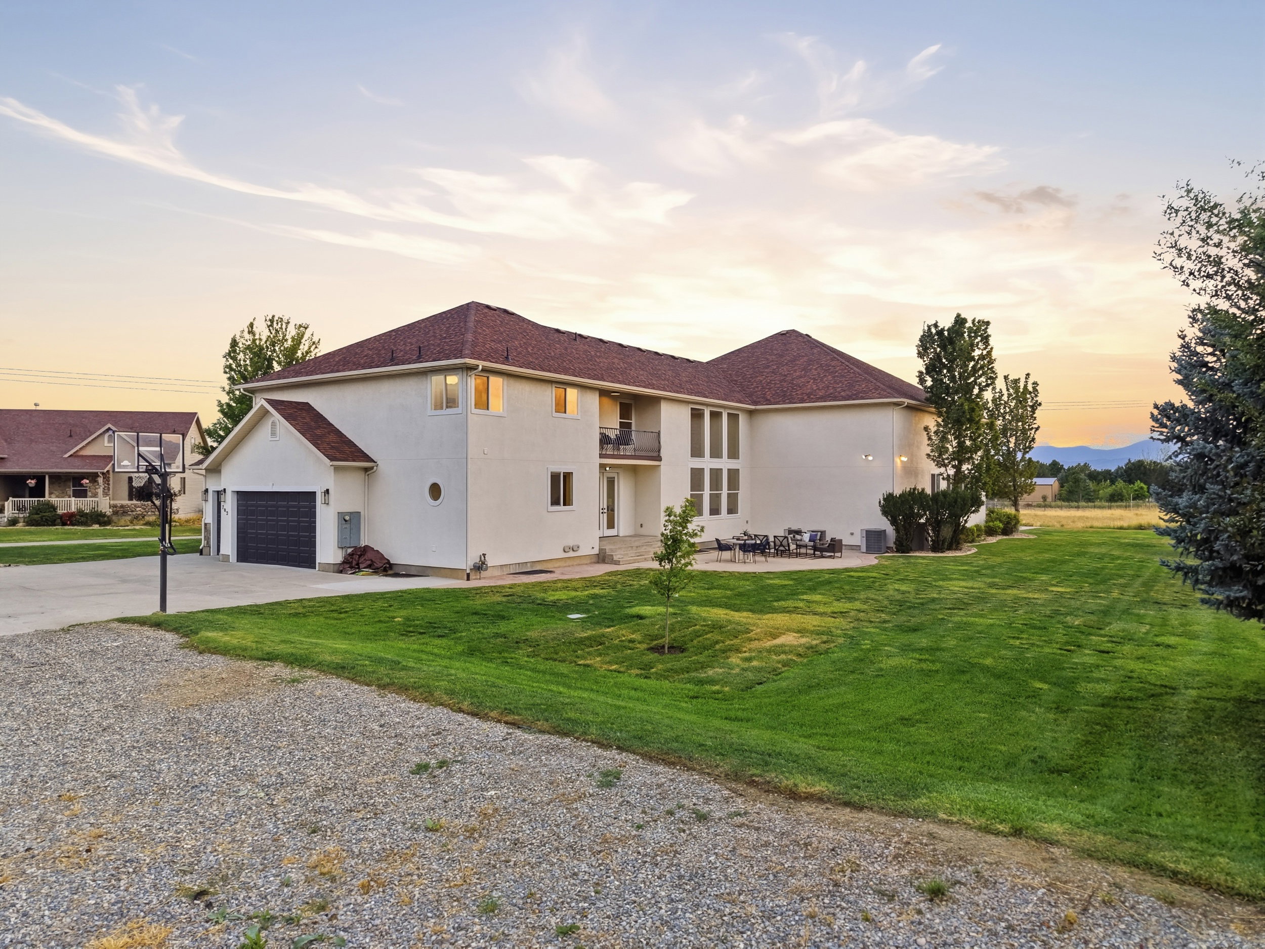 Spacious two-story residence featuring a gravel driveway, attached garage, large rear patio, and expansive green lawn