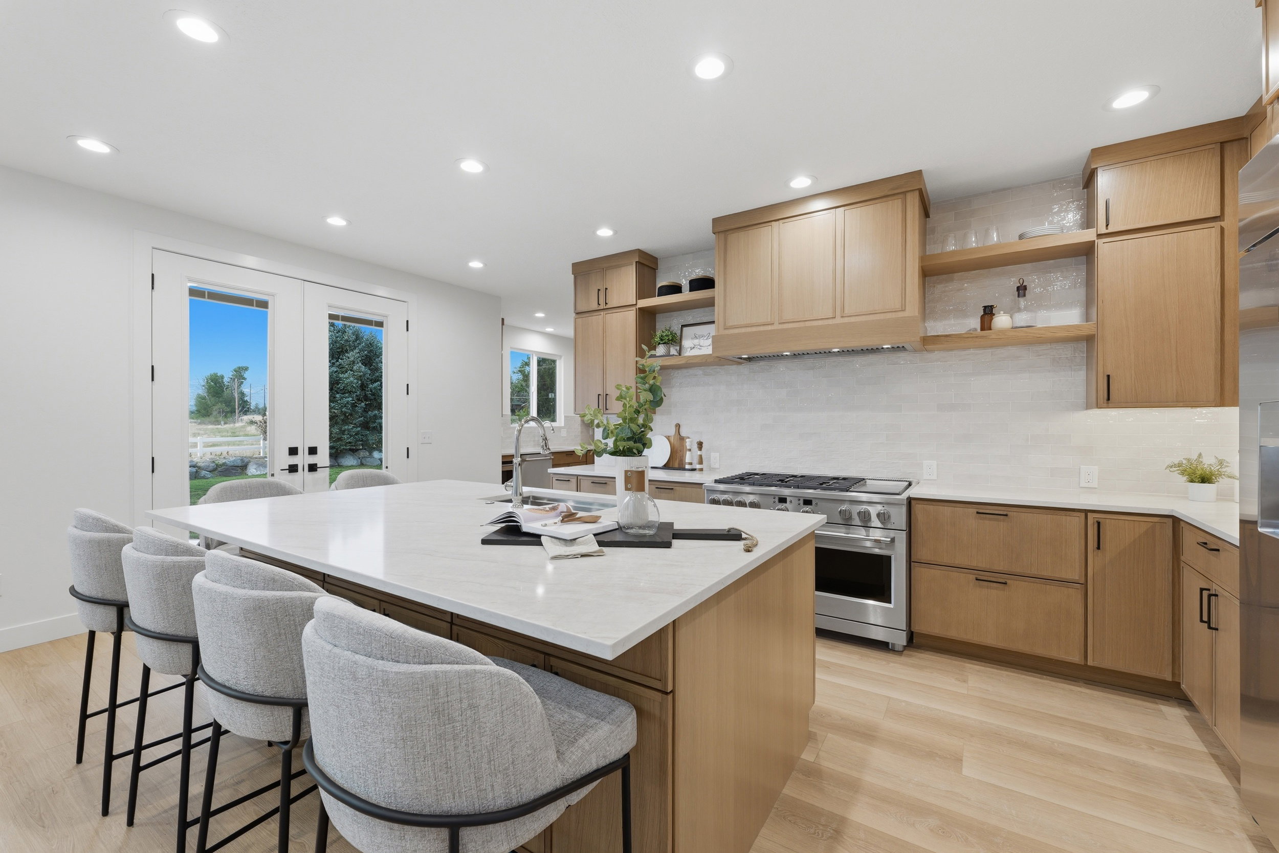 Kitchen featuring a large central island with a sink, light wood-finish cabinetry, stainless steel range with matching hood, light stone countertops, and recessed lighting