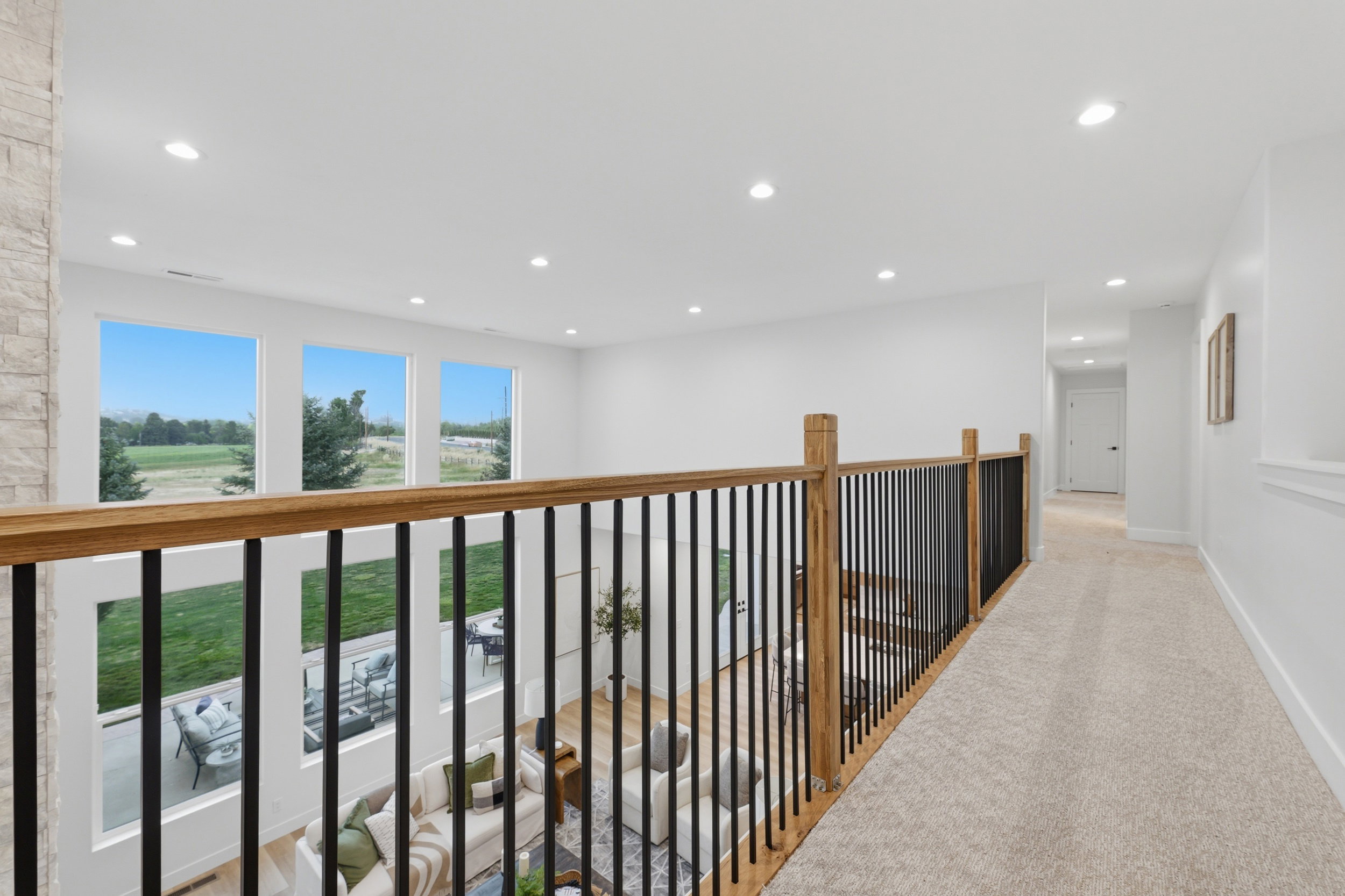 Open-concept upper-level hallway featuring a light wood railing with black metal spindles and recessed lighting