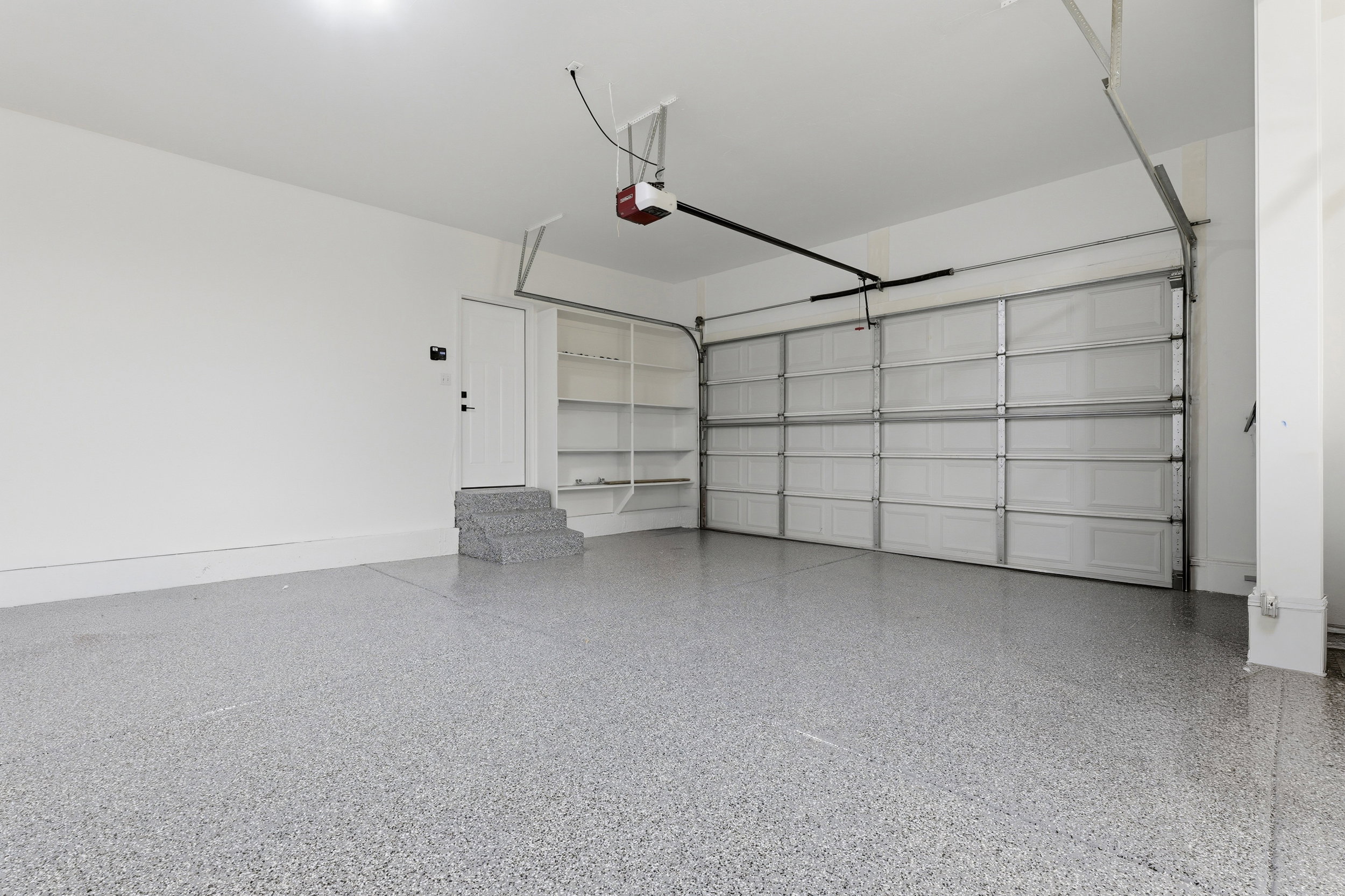 Spacious garage featuring a durable epoxy-coated floor, automatic garage door opener, built-in shelving, and a service door for interior access