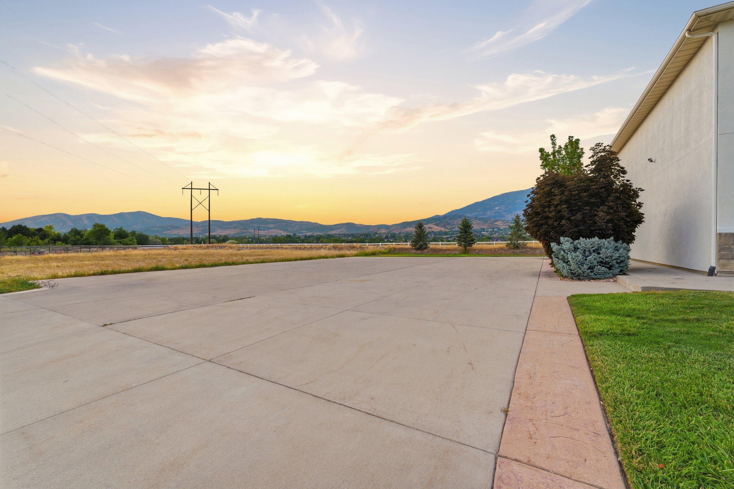 Expansive concrete paving with a landscape border, manicured lawn, and mature plantings