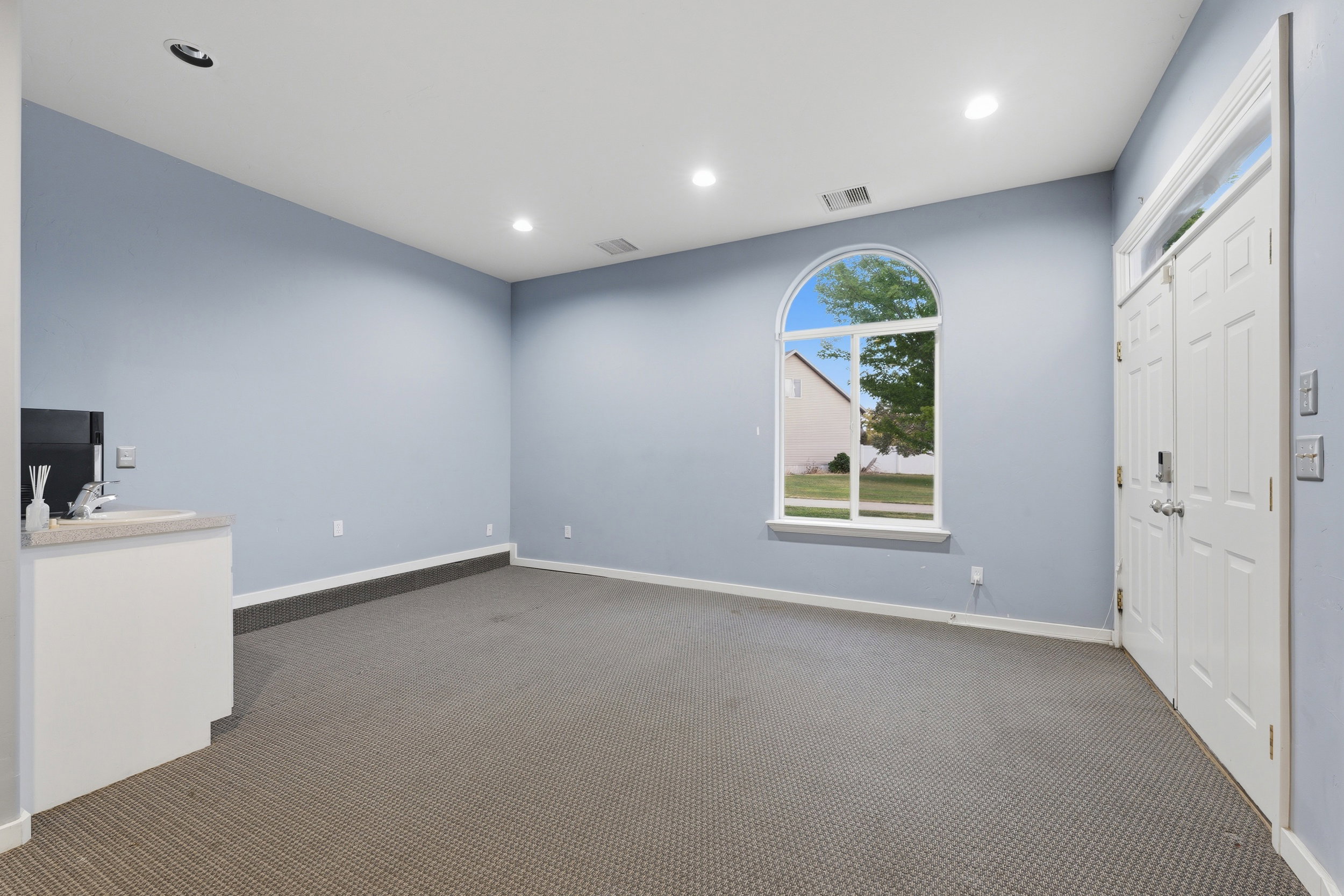 Spacious interior room featuring a large arched window, recessed lighting, and a built-in wet bar with a sink and countertop
