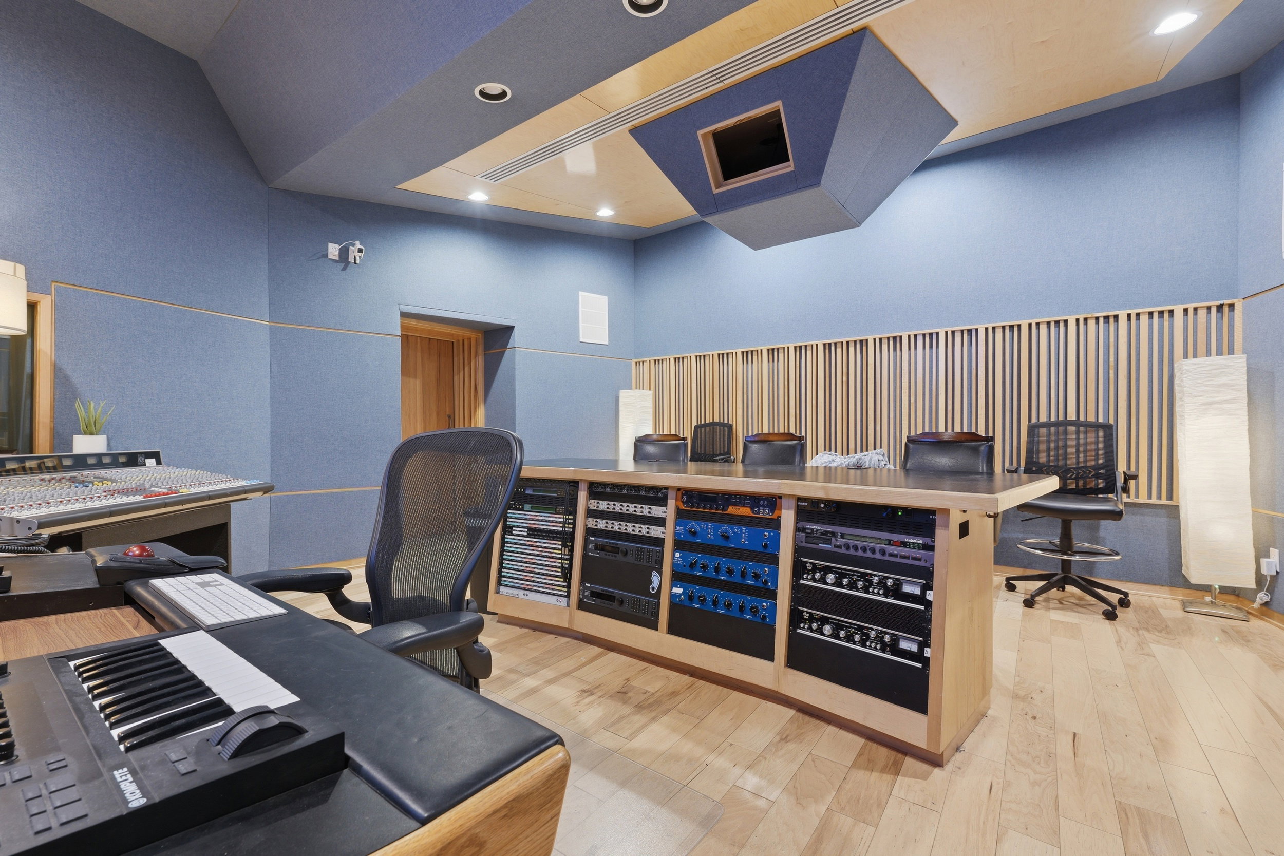 Dedicated studio space featuring acoustic paneling on walls and ceiling, wood-finish flooring, recessed lighting, a built-in sound mixing desk with integrated equipment racks, and a wood slat acoustic wall treatment